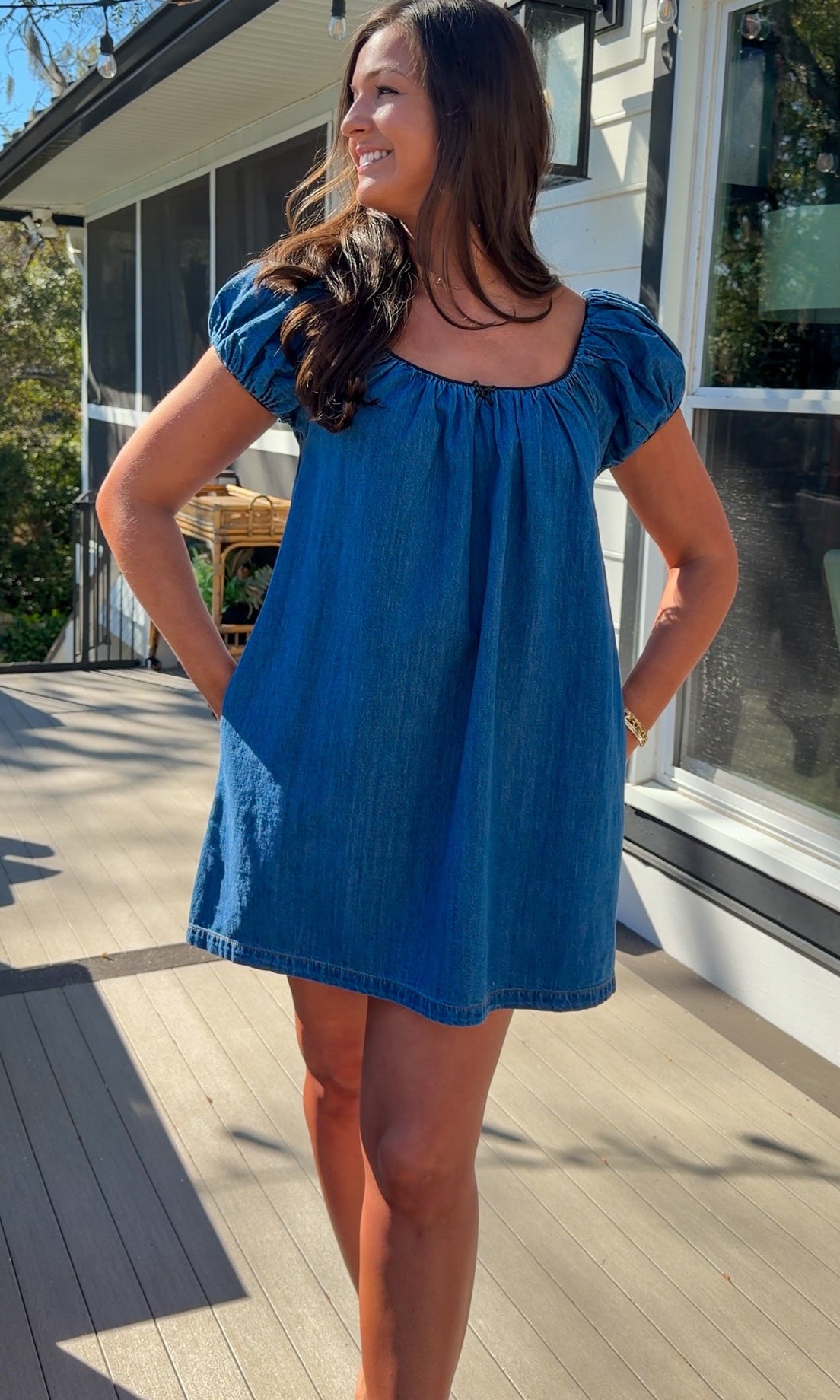 Blue denim mini dress with scoop neckline, short puff sleeves, and relaxed babydoll fit, worn outdoors in natural light.