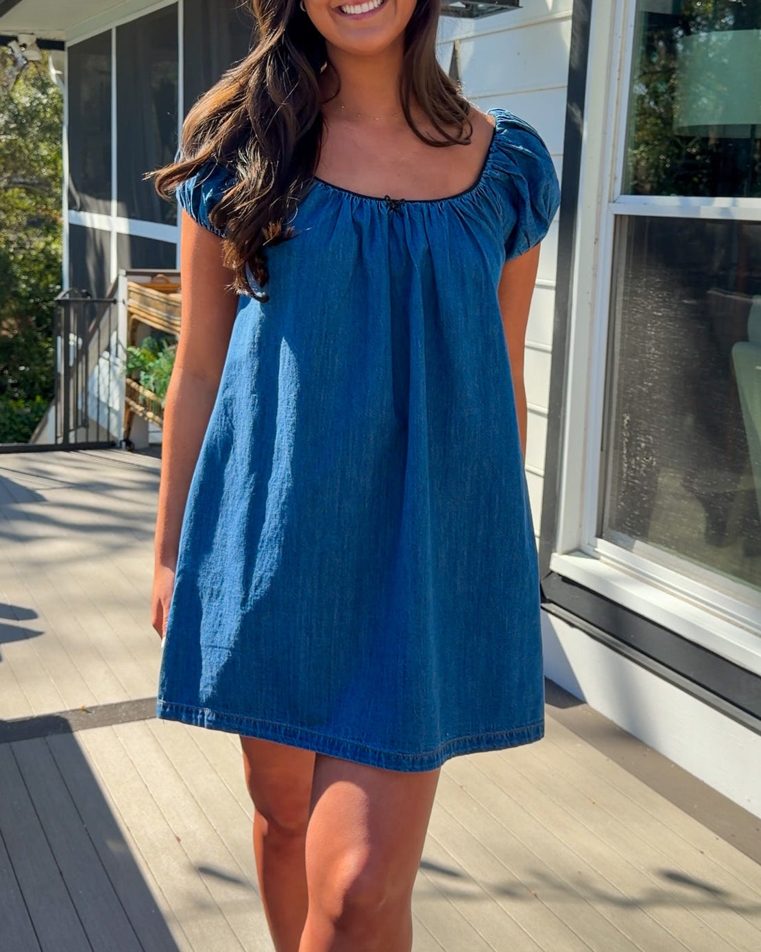 Blue denim mini dress with scoop neckline, short puff sleeves, and relaxed babydoll fit, worn outdoors in natural light.