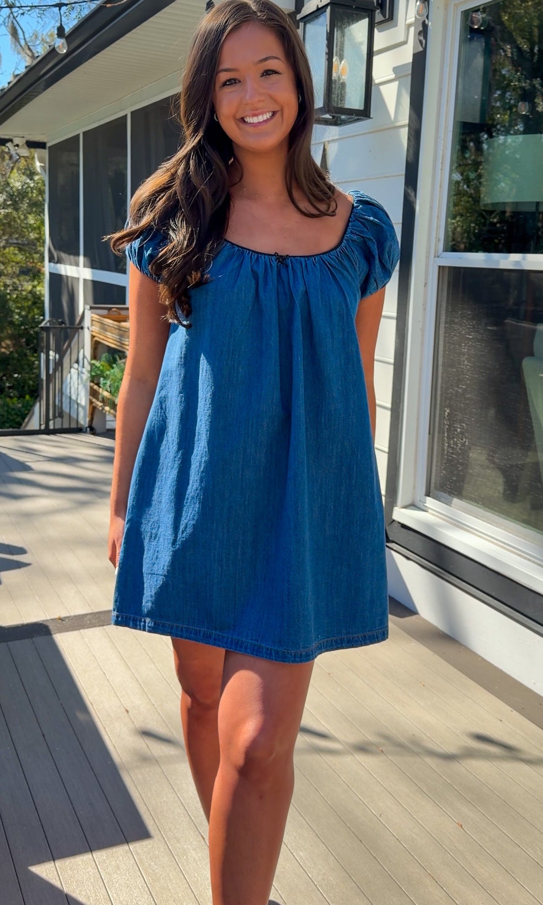Blue denim mini dress with scoop neckline, short puff sleeves, and relaxed babydoll fit, worn outdoors in natural light.