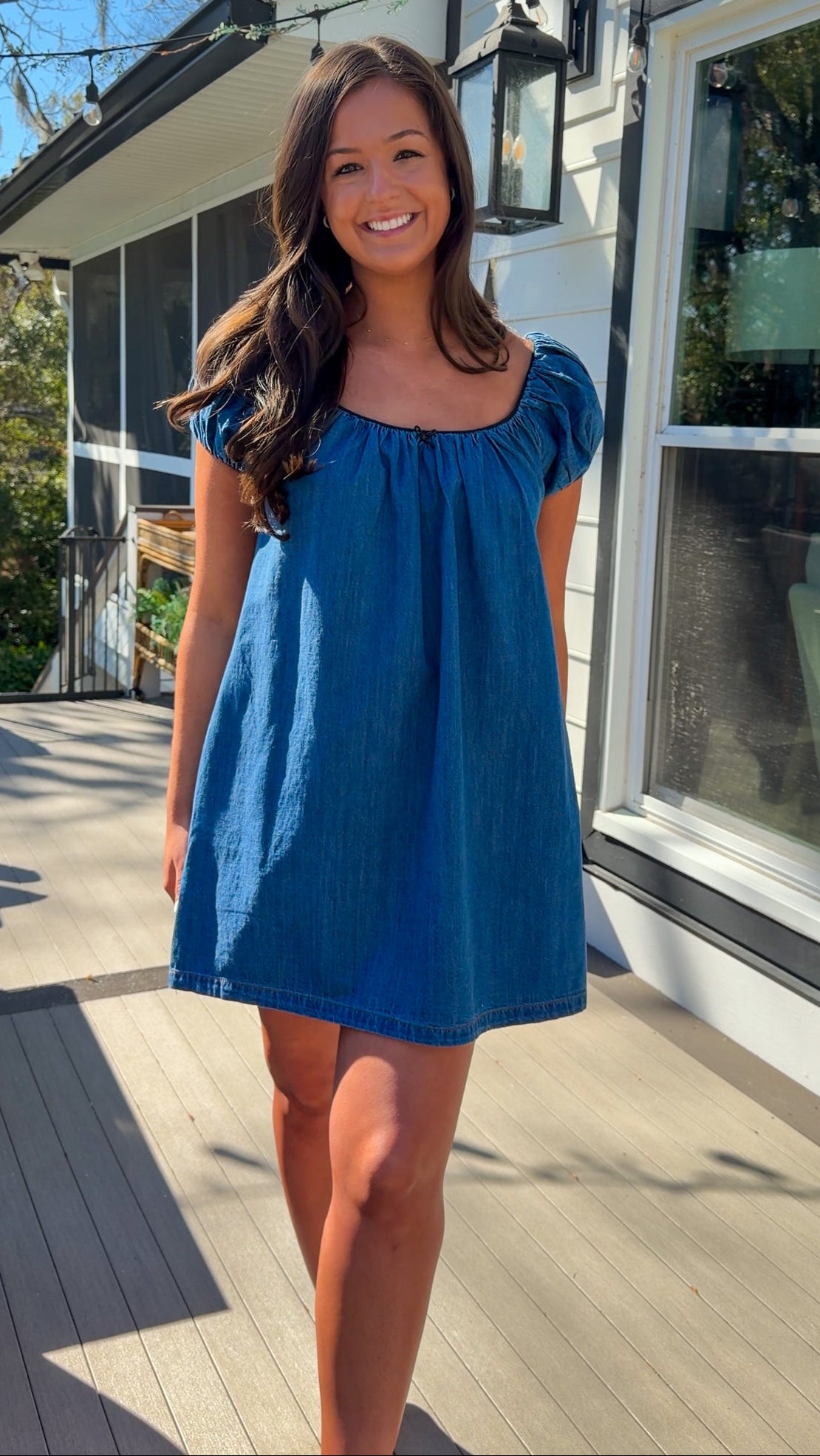 Blue denim mini dress with scoop neckline, short puff sleeves, and relaxed babydoll fit, worn outdoors in natural light.