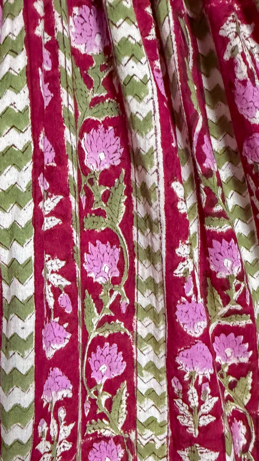 A close-up of a fabric with vertical stripes featuring magenta, olive green, and white patterns including floral motifs, chevron stripes, and leafy vines.