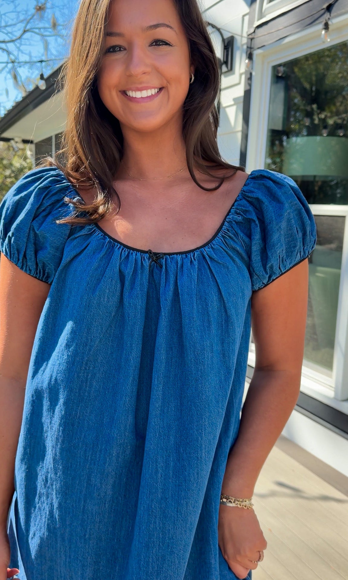 Blue denim mini dress with scoop neckline, short puff sleeves, and relaxed babydoll fit, worn outdoors in natural light.