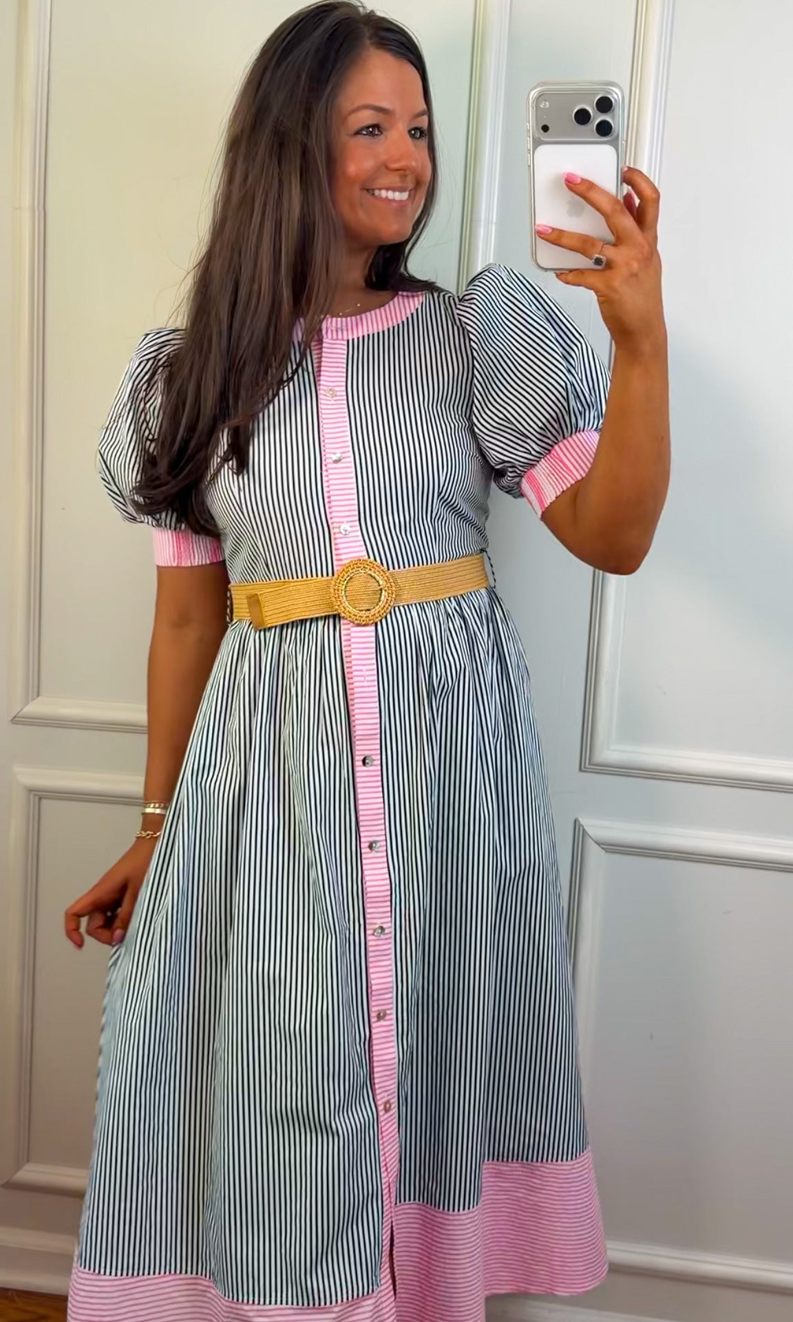 Woman taking a mirror selfie wearing a striped dress with pink accents and a yellow belt.