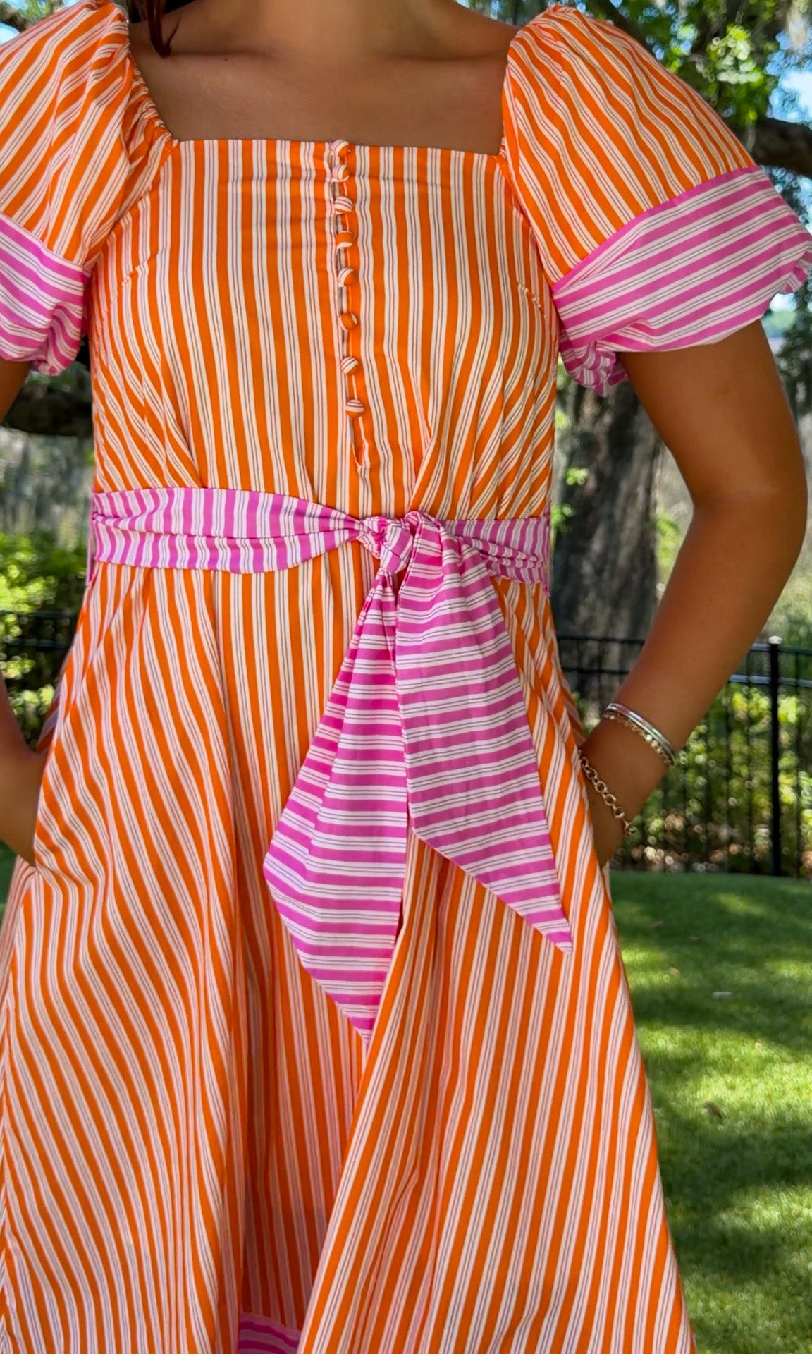 Person wearing an orange and pink striped dress with a blurred outdoor background