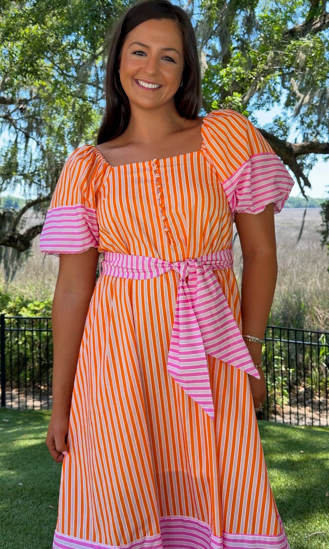 Woman wearing an orange and pink striped dress with a garden background