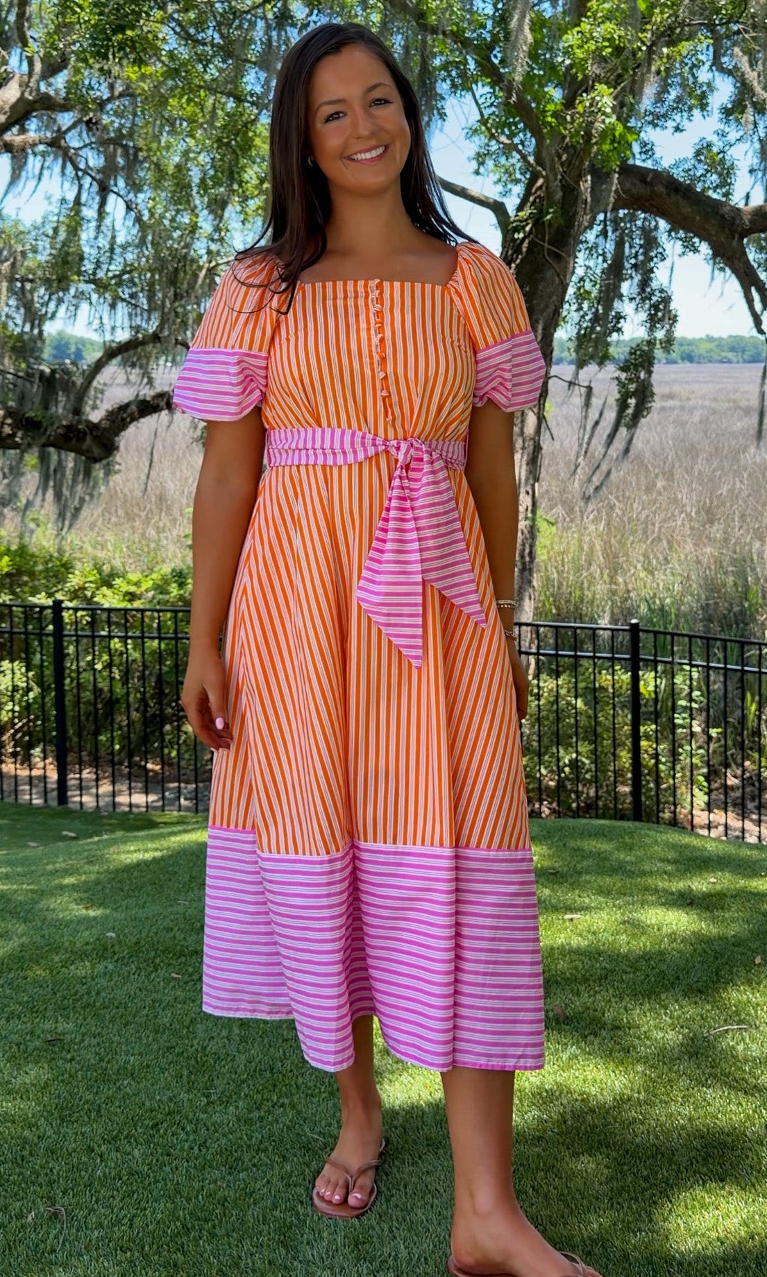 Woman wearing a striped dress standing outdoors with trees and grass in the background