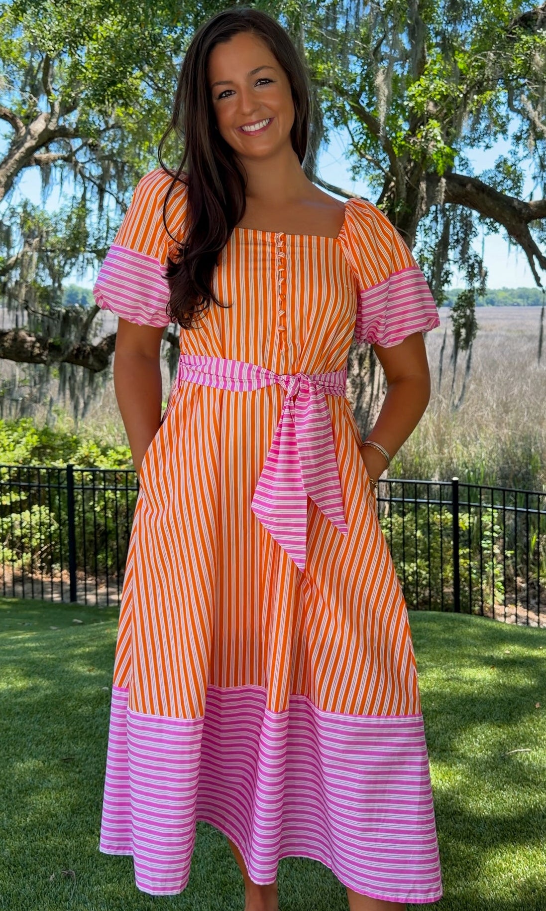Woman wearing a colorful striped dress standing outdoors with trees and grass in the background