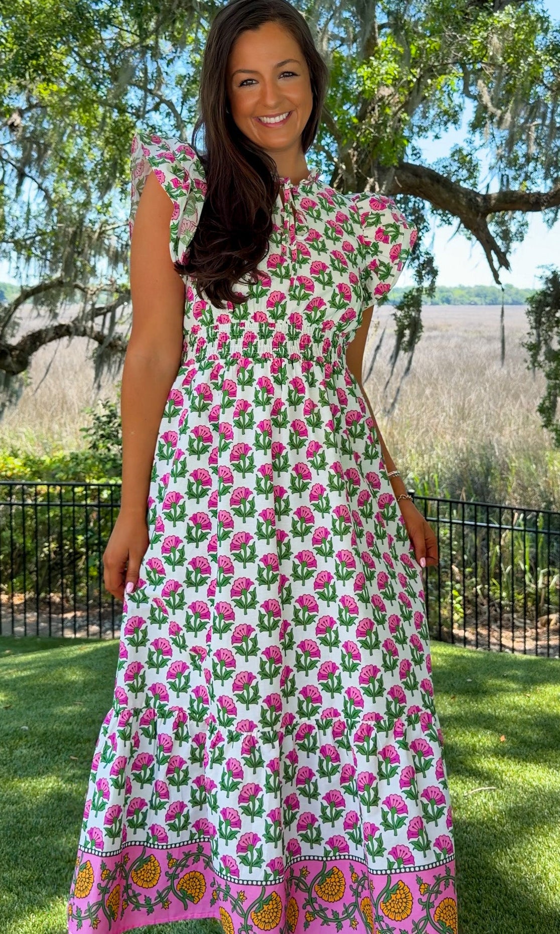 Woman wearing a floral dress standing outdoors with trees and grass in the background