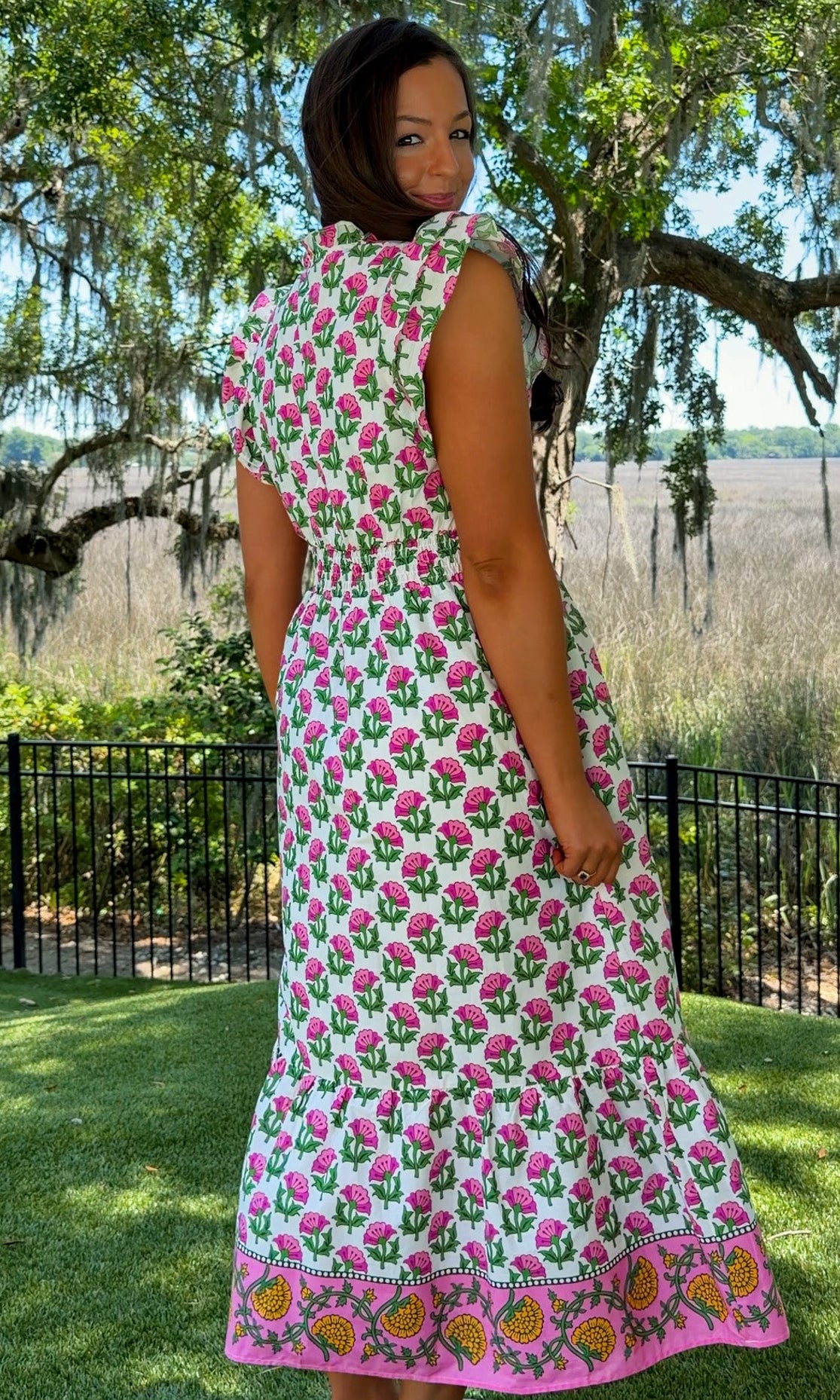 Woman in a floral dress standing outdoors with trees and grass in the background