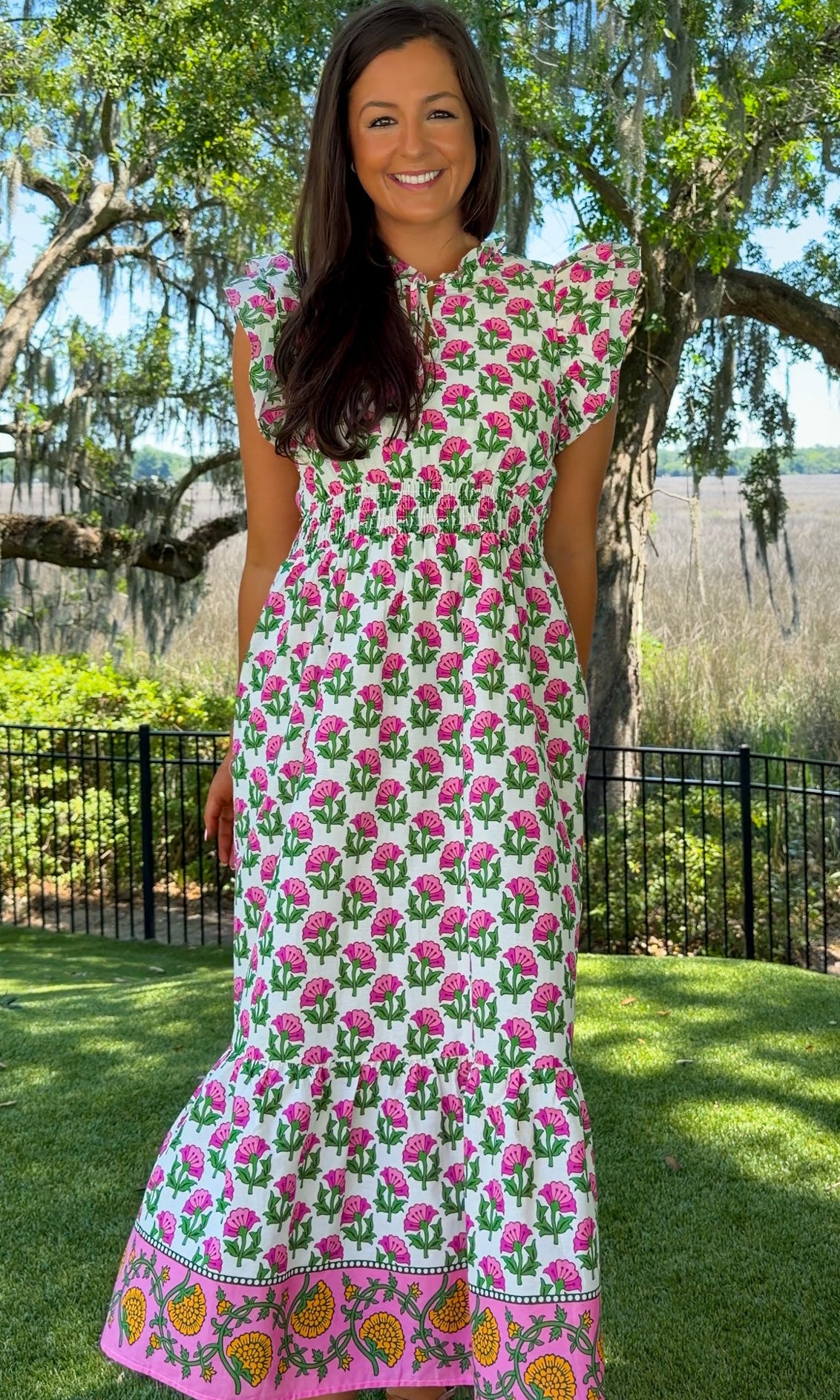 Woman wearing a floral dress standing outdoors with trees and grass in the background