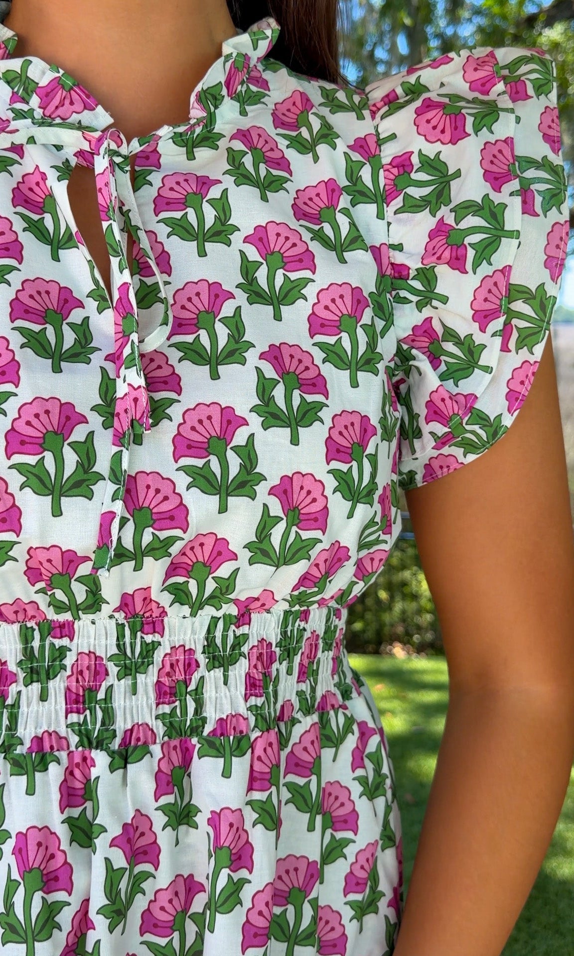 Person wearing a floral dress with pink and green flowers in an outdoor setting