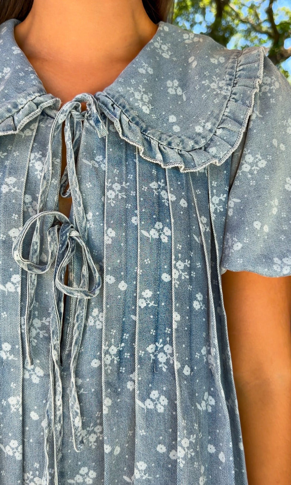 Close-up of a person wearing a blue floral dress with a ruffled collar.