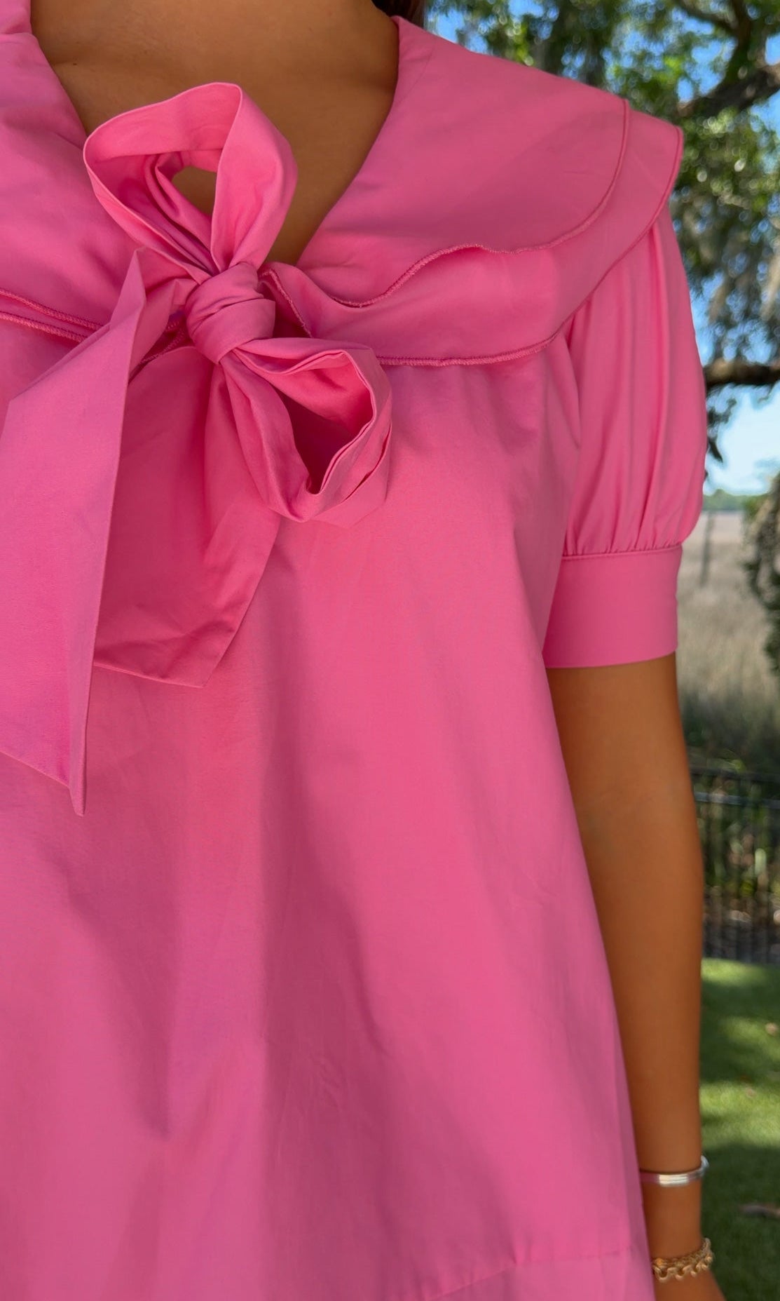 Close-up of a pink dress with a bow detail, worn outdoors.