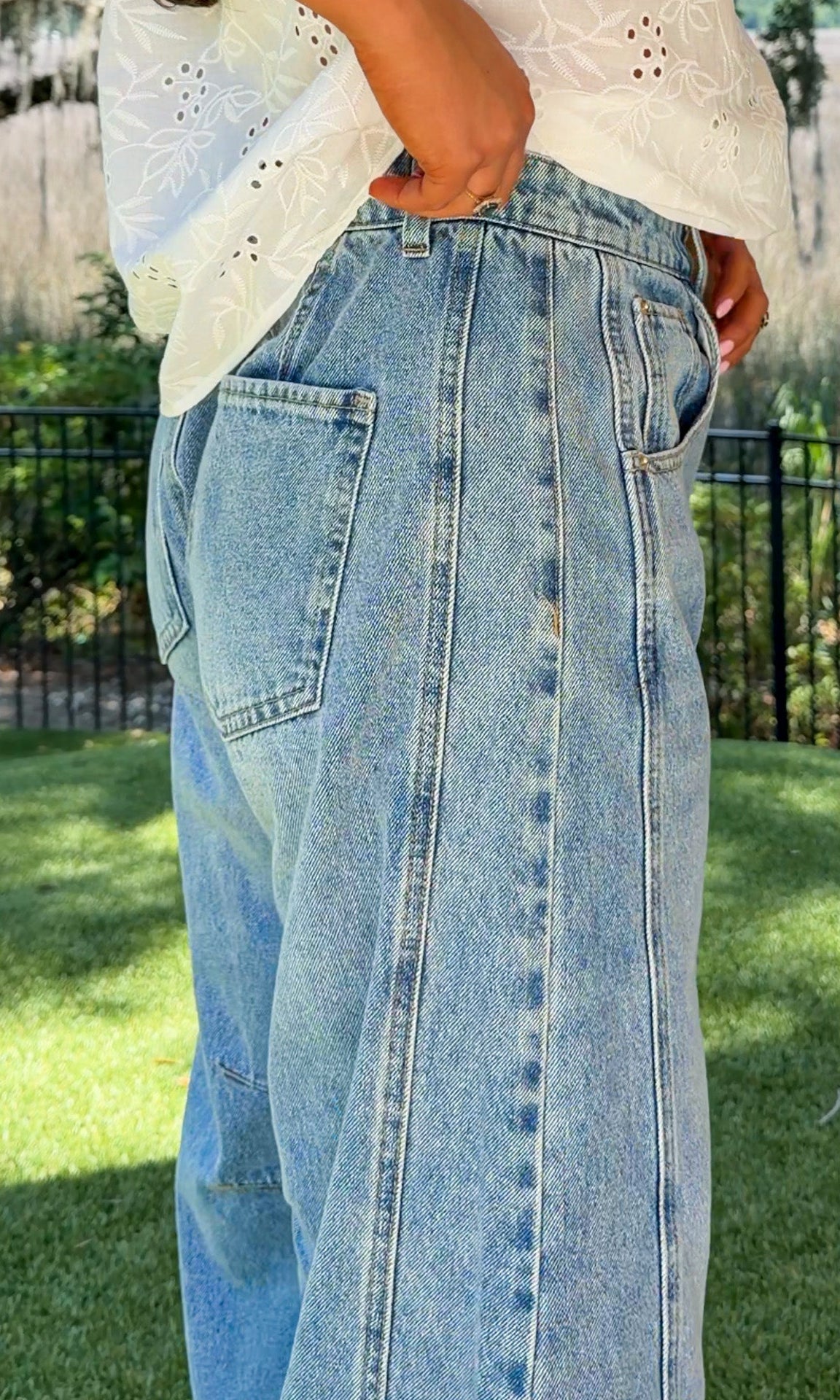 Person wearing light blue jeans and a white top outdoors on a sunny day.