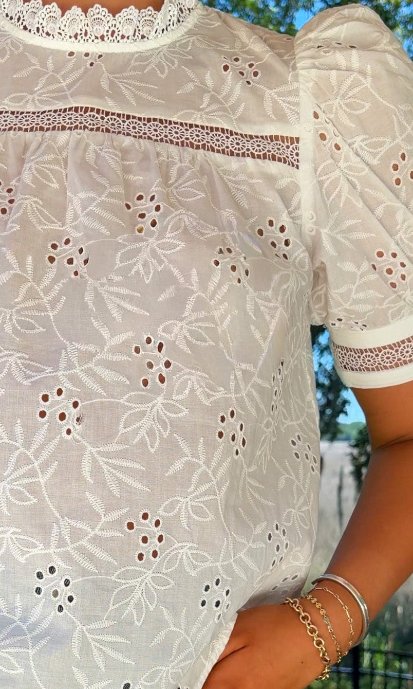 Person wearing a white lace blouse with short sleeves and blue jeans outdoors.