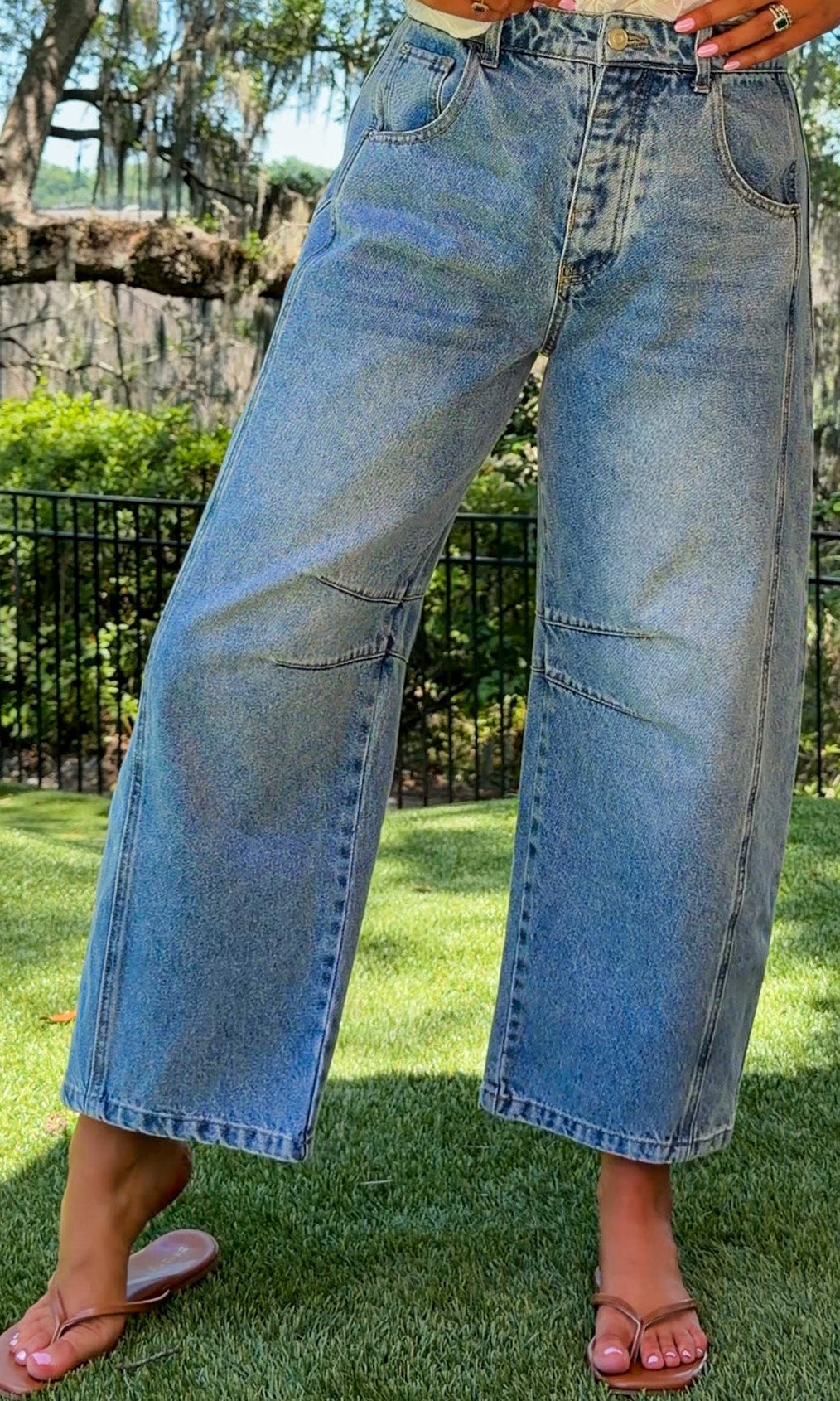Person wearing light blue jeans and a white top standing on grass with trees in the background
