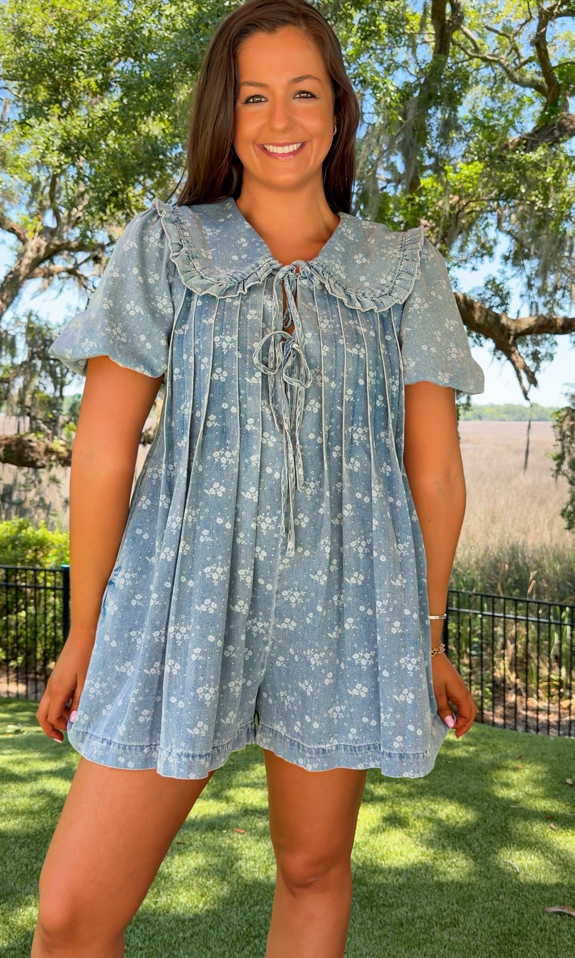 Woman wearing a blue floral dress standing outdoors with trees and grass in the background