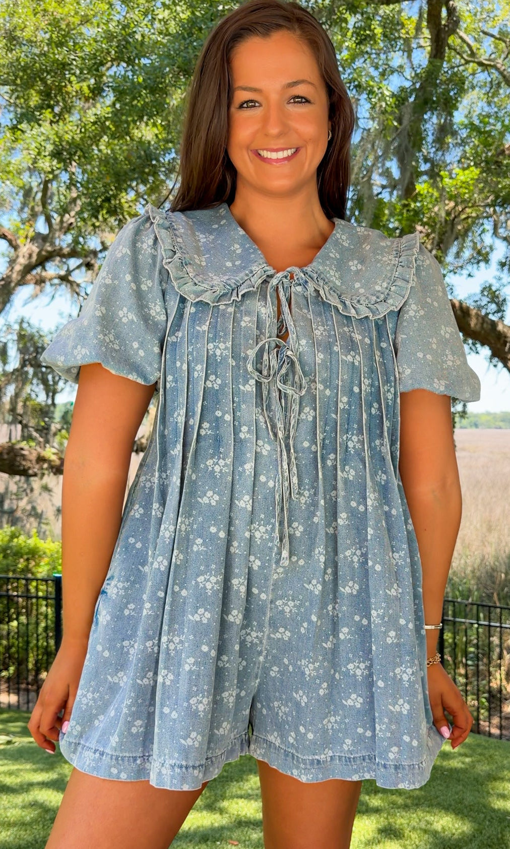 Woman wearing a blue floral dress standing outdoors with trees and grass in the background