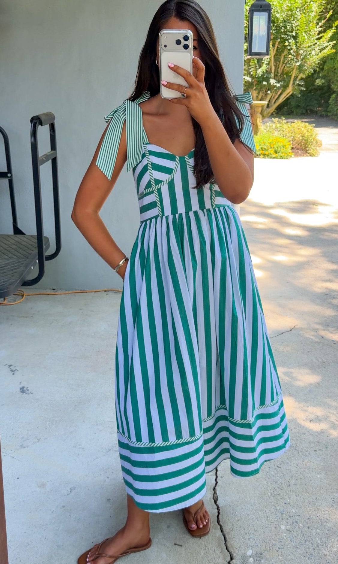 Woman wearing a green and white striped dress taking a mirror selfie outdoors.