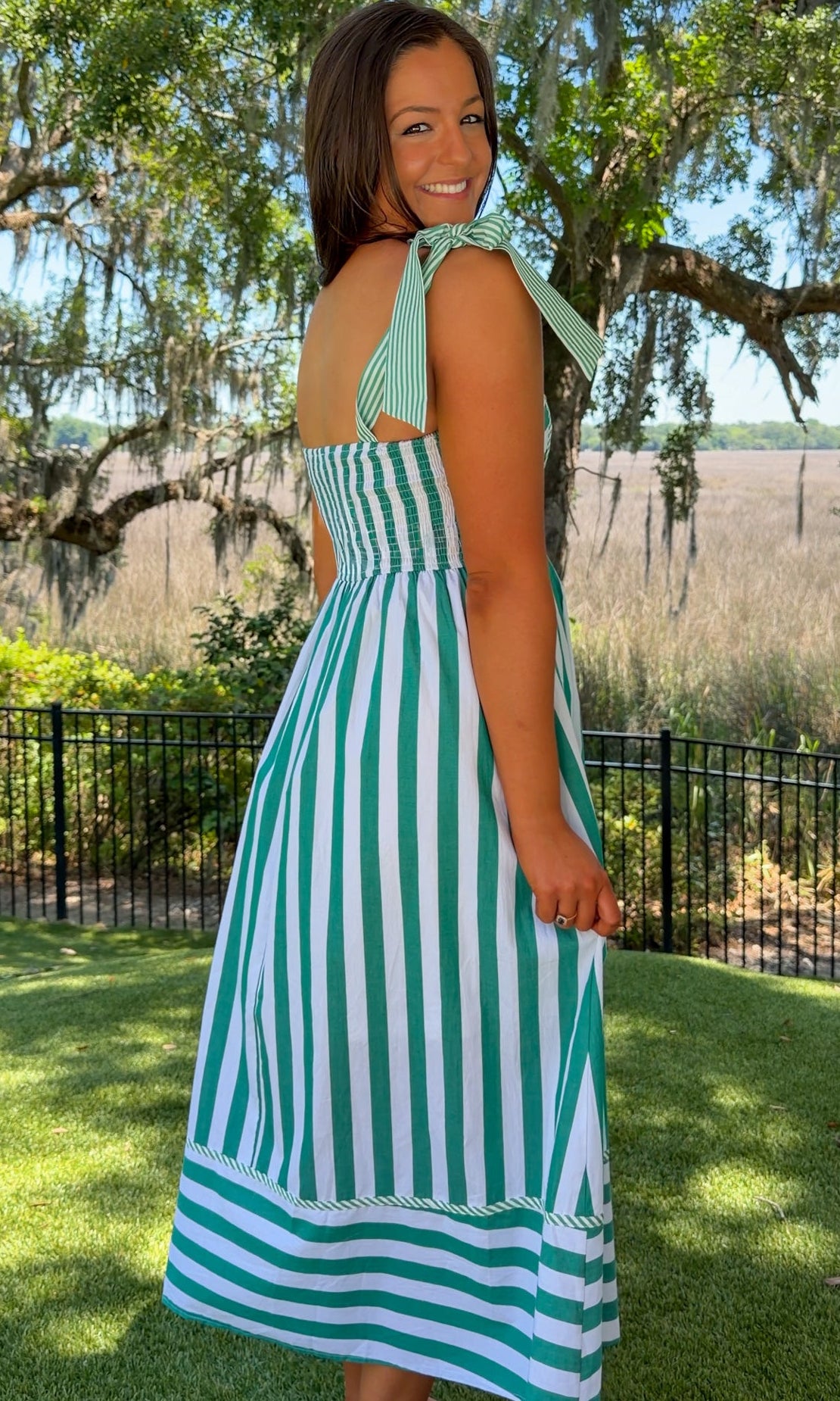 Woman wearing a green and white striped dress standing outdoors with trees and grass in the background