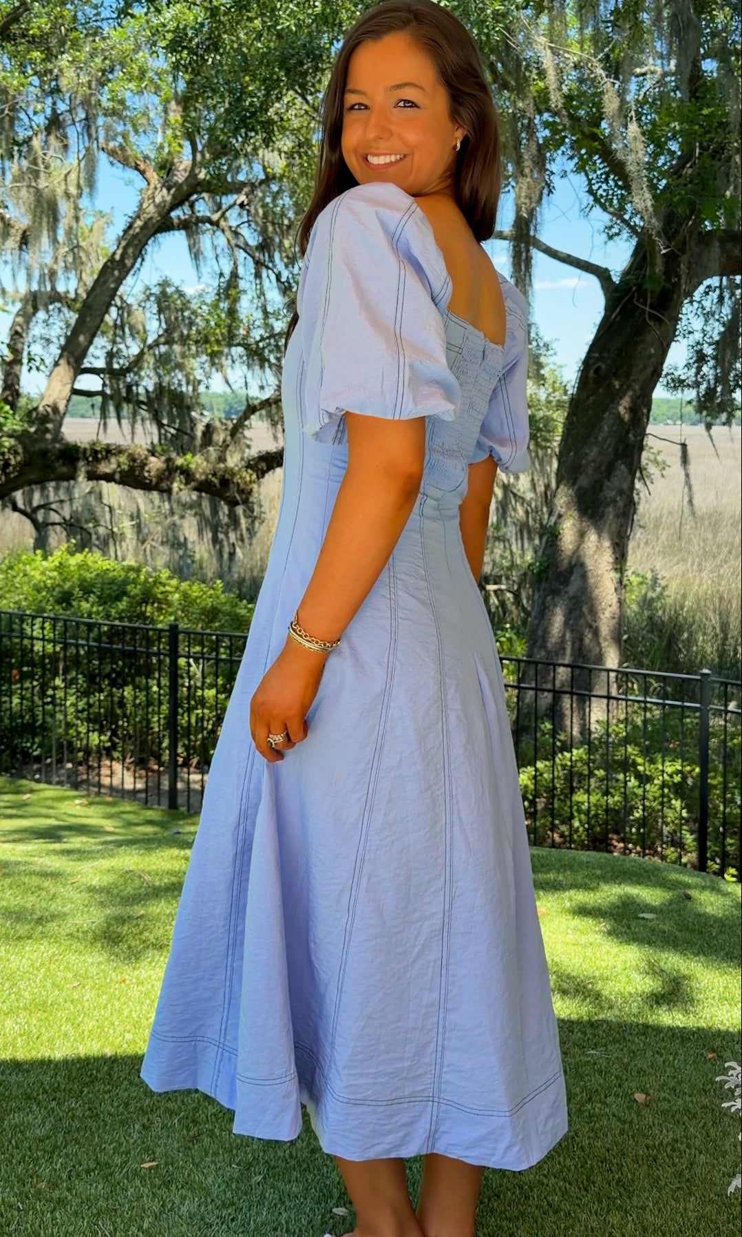 Woman in a light blue dress standing outdoors with trees and grass in the background