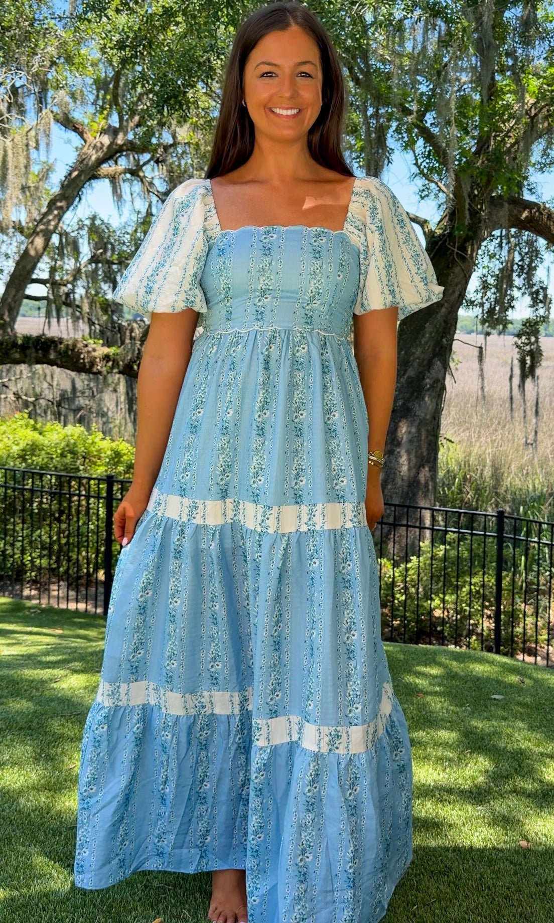 Woman in a blue dress standing outdoors with trees and grass in the background