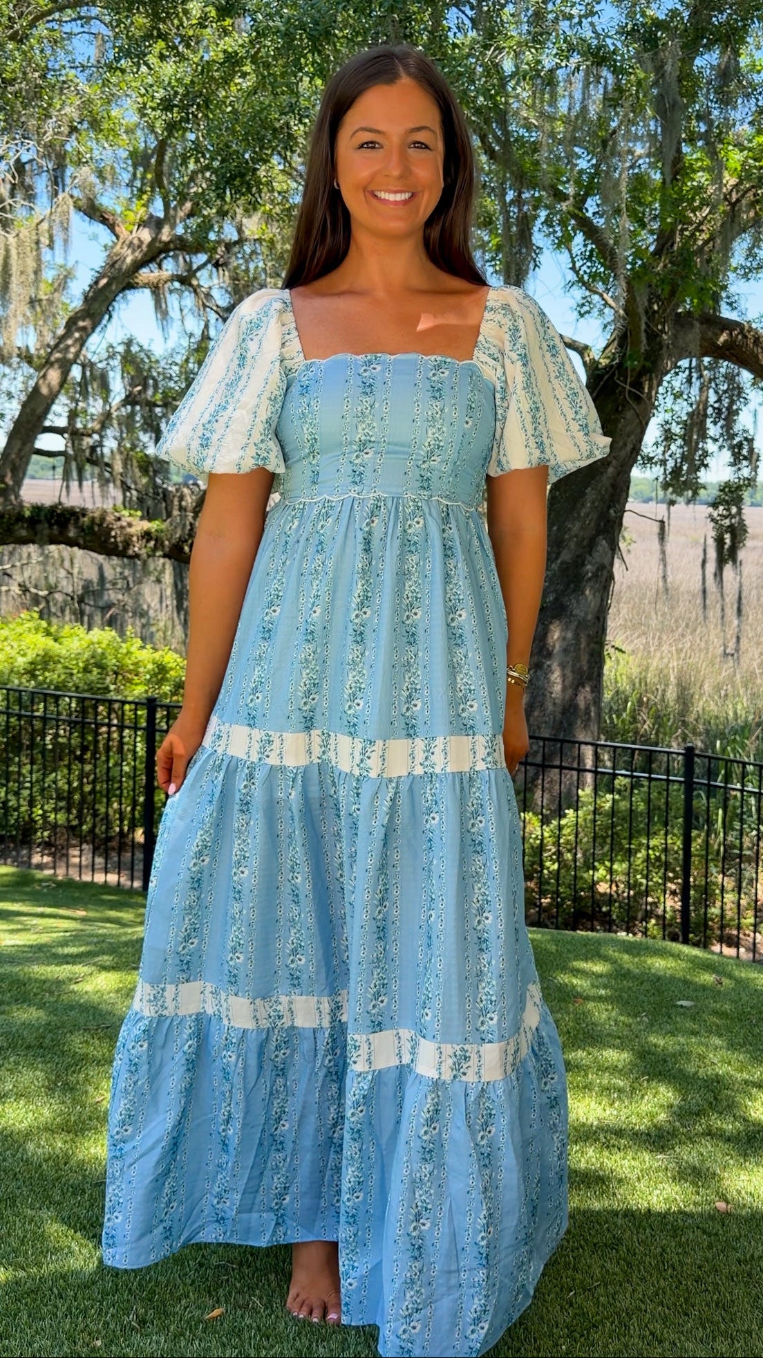 Woman in a blue dress standing outdoors with trees and grass in the background