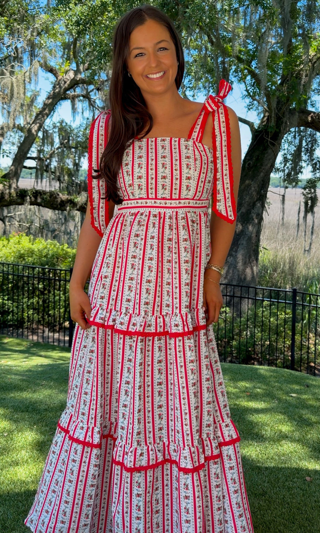 Woman in a red and white dress standing outdoors with trees and grass in the background