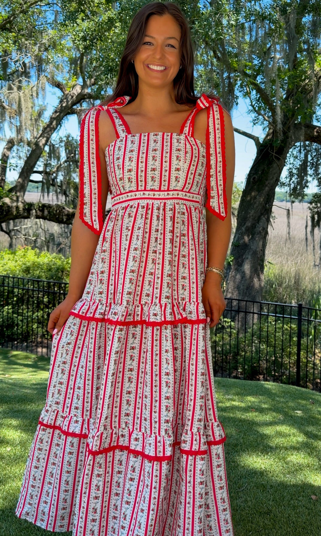 Woman wearing a red and white patterned dress standing outdoors with trees and grass in the background