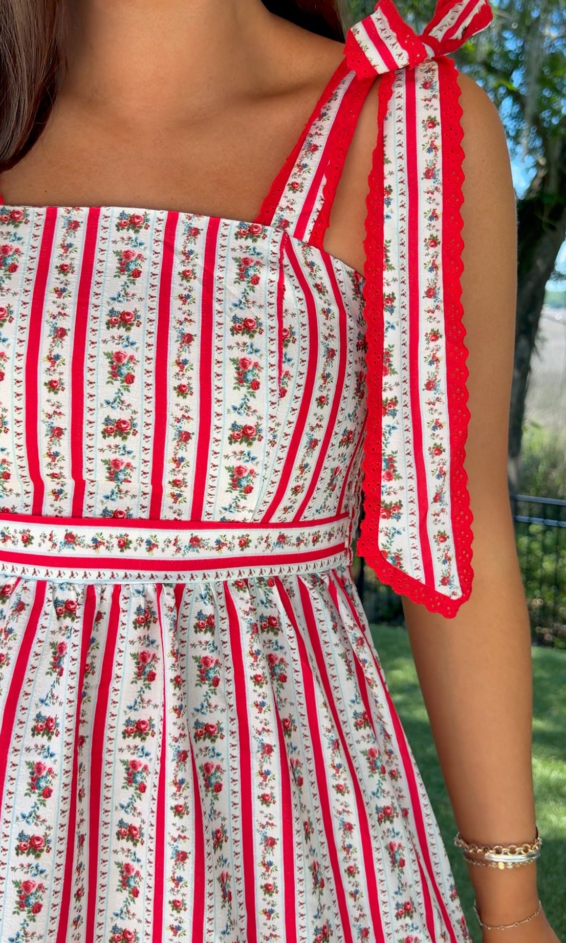 Woman wearing a red and white patterned dress with floral details outdoors.