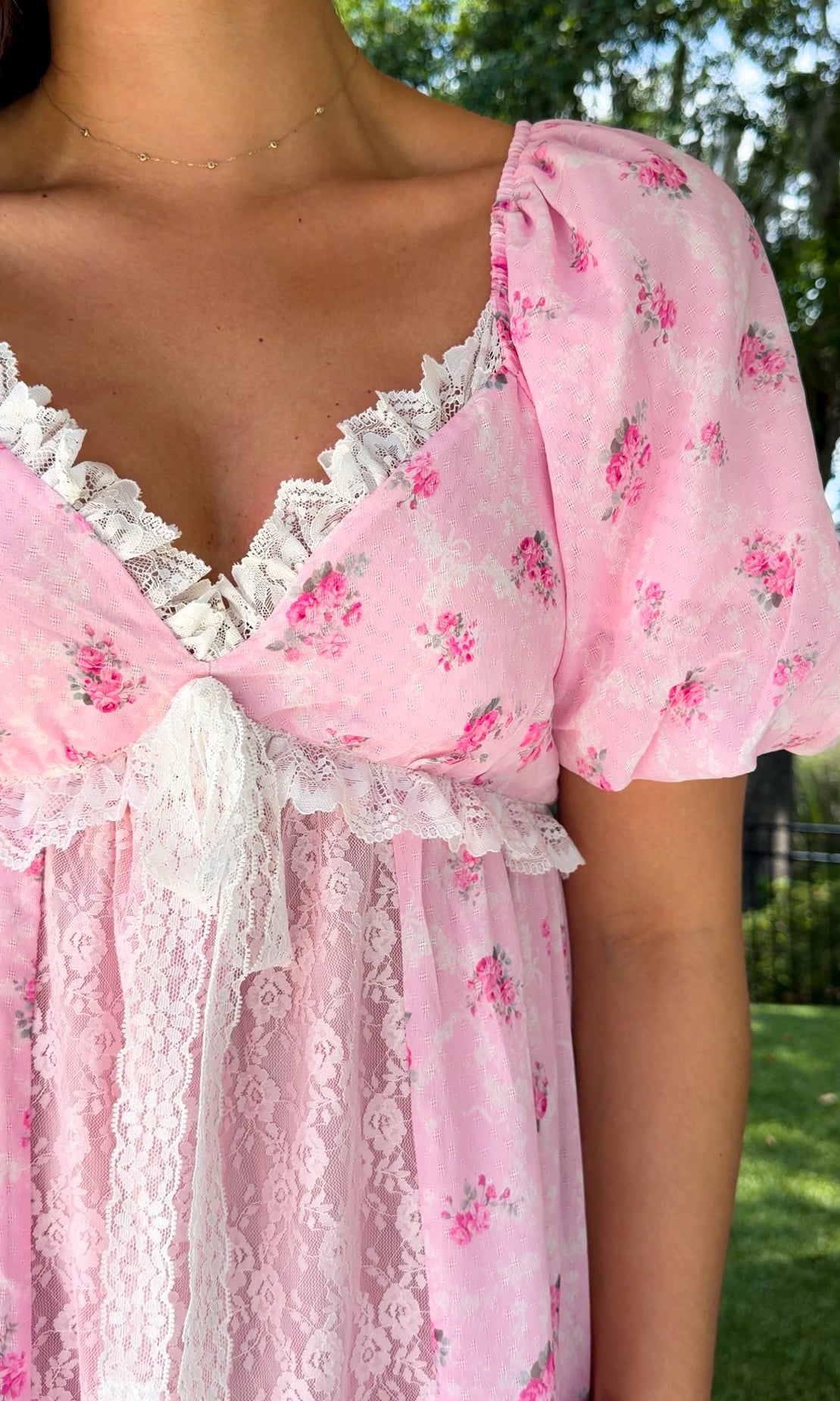 Pink floral maxi dress with delicate rose print, lace-trimmed V-neckline, puff short sleeves, empire waist, smocked back, and tiered skirt with lace panel details