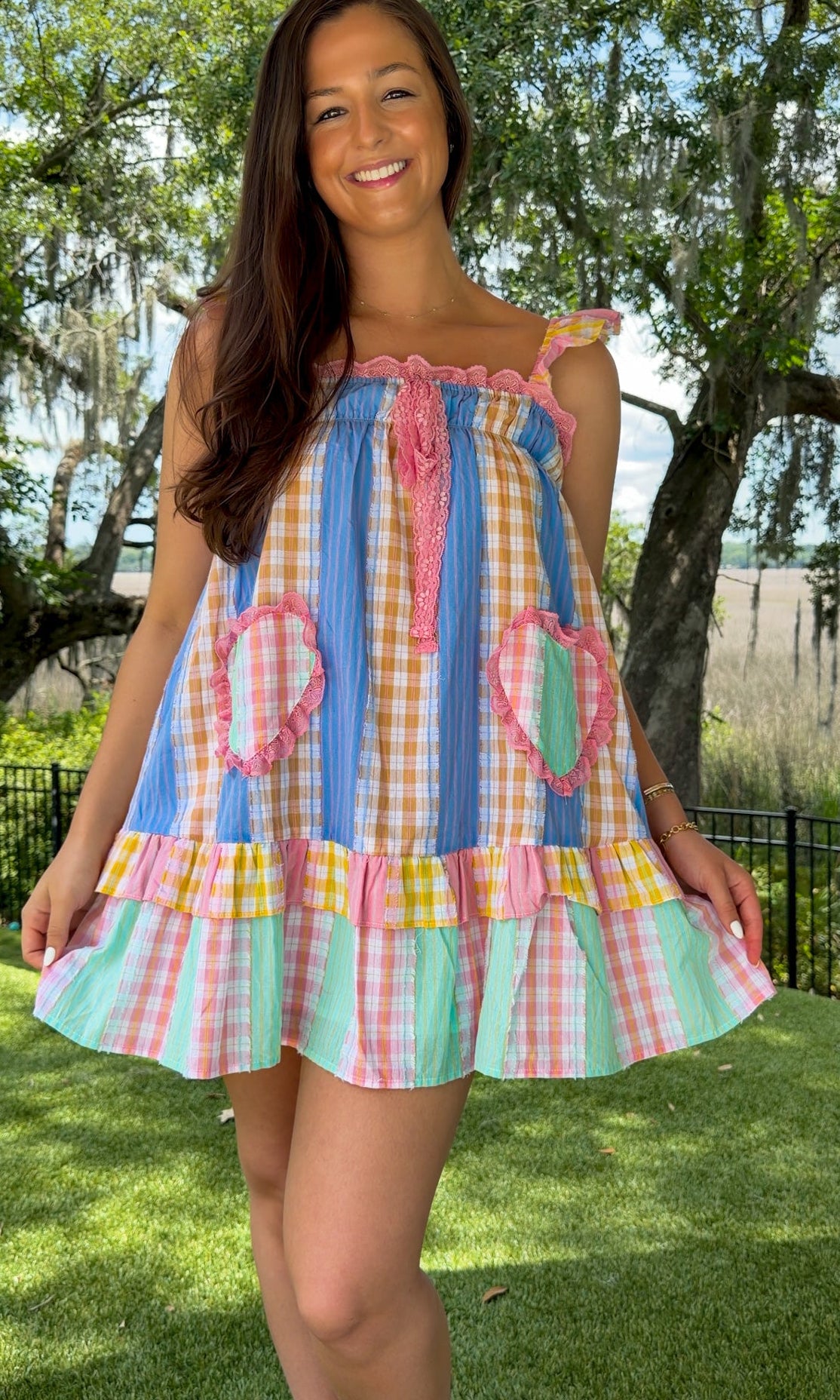 Pastel patchwork mini dress featuring mixed check and stripe prints in pink, blue, yellow, and mint with ruffle straps, heart-shaped front pockets, pink lace trim, and a relaxed babydoll silhouette.