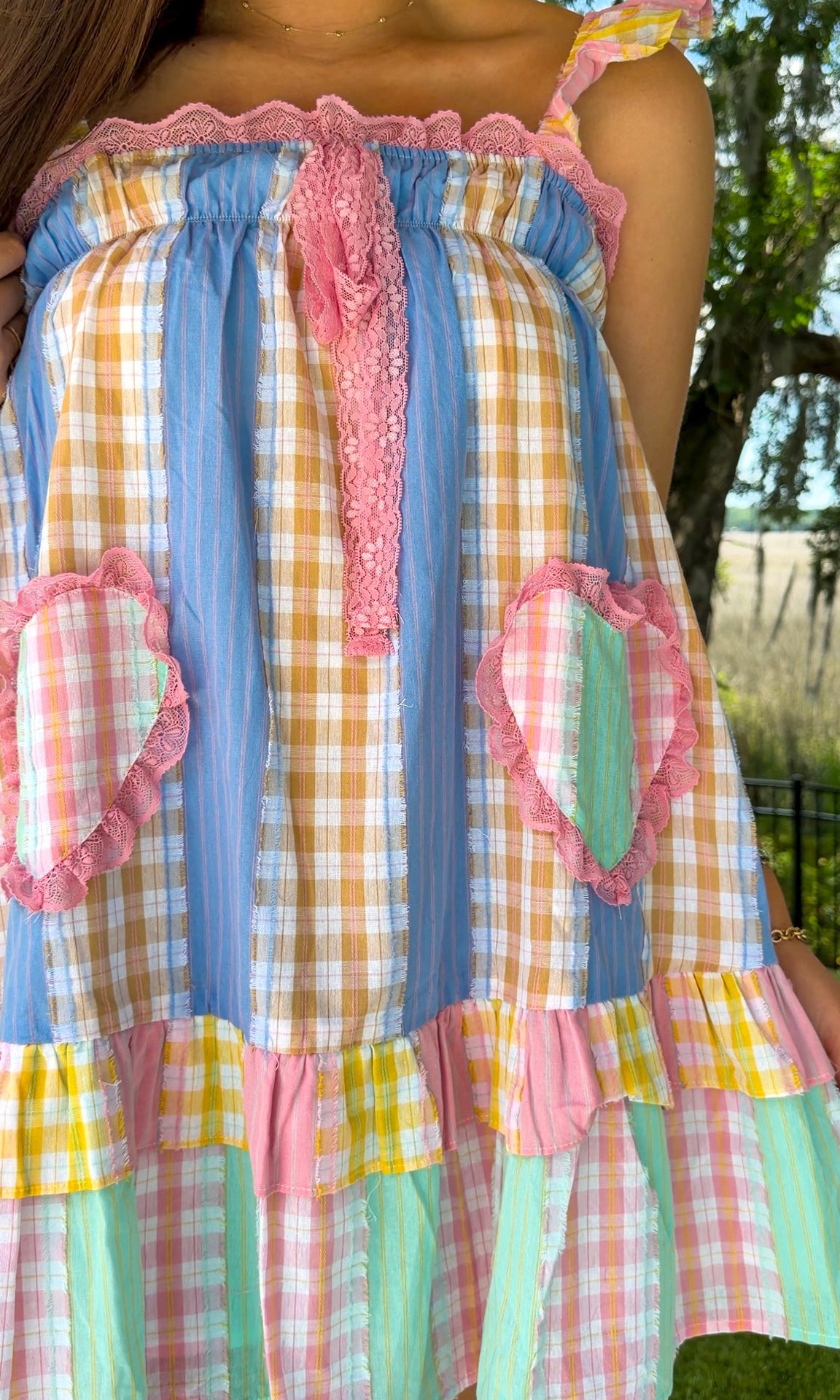 Pastel patchwork mini dress featuring mixed check and stripe prints in pink, blue, yellow, and mint with ruffle straps, heart-shaped front pockets, pink lace trim, and a relaxed babydoll silhouette.