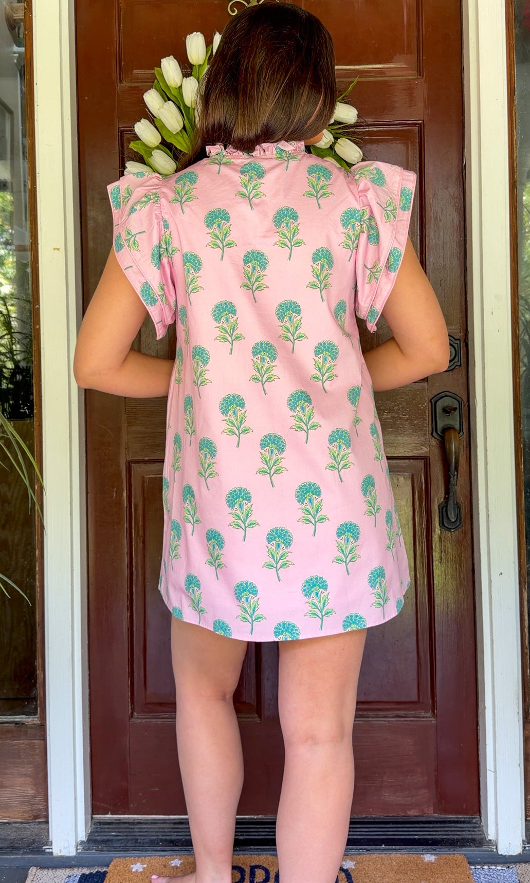 Pink and green floral mini dress with flutter sleeves, a ruffled stand neckline, decorative frog button closures, and a relaxed shift silhouette.