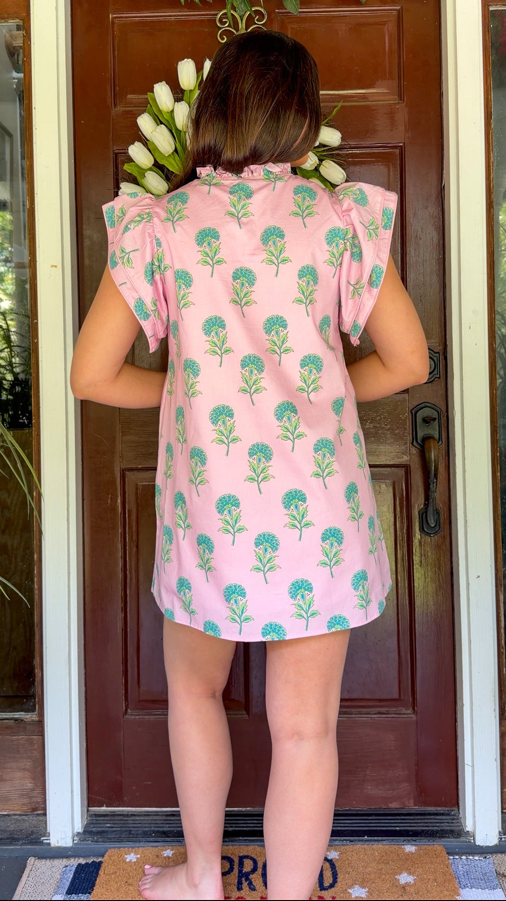 Pink and green floral mini dress with flutter sleeves, a ruffled stand neckline, decorative frog button closures, and a relaxed shift silhouette.