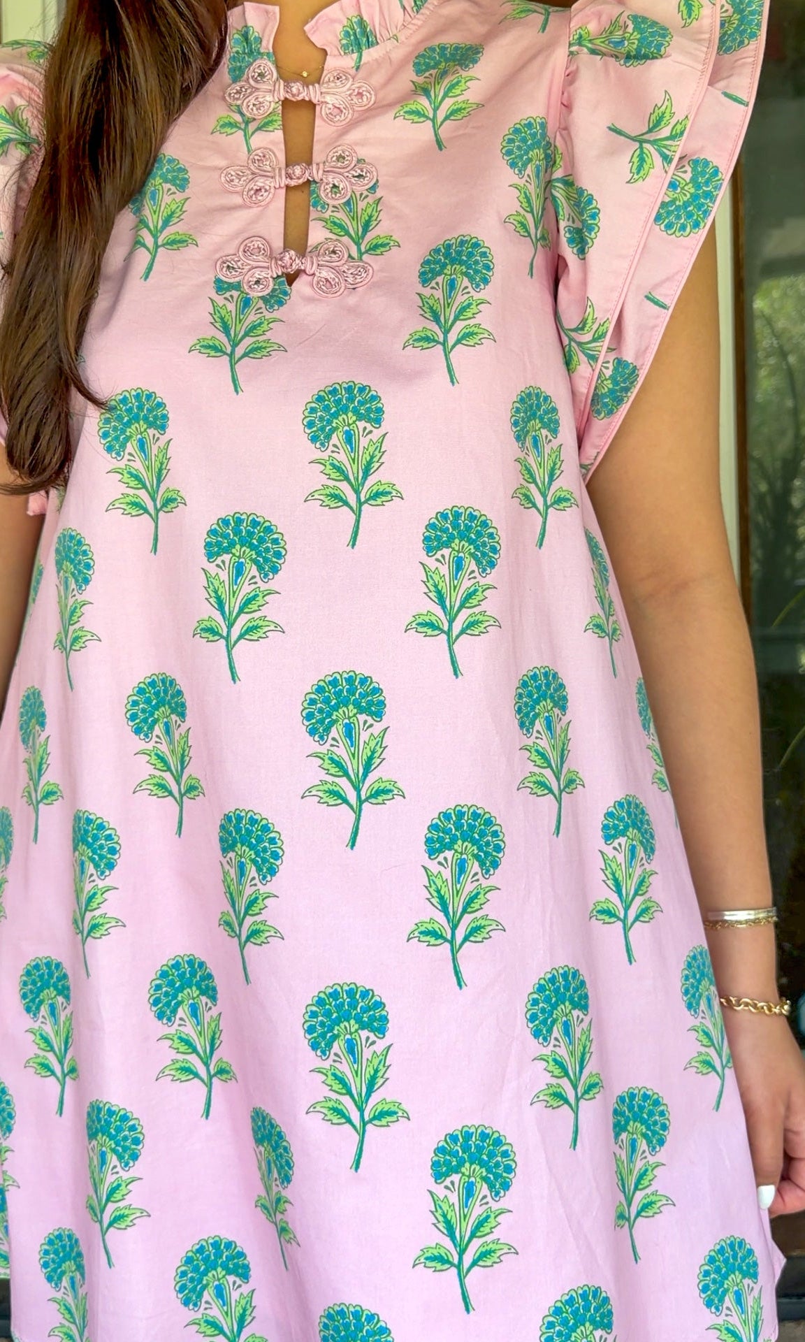 Pink and green floral mini dress with flutter sleeves, a ruffled stand neckline, decorative frog button closures, and a relaxed shift silhouette.