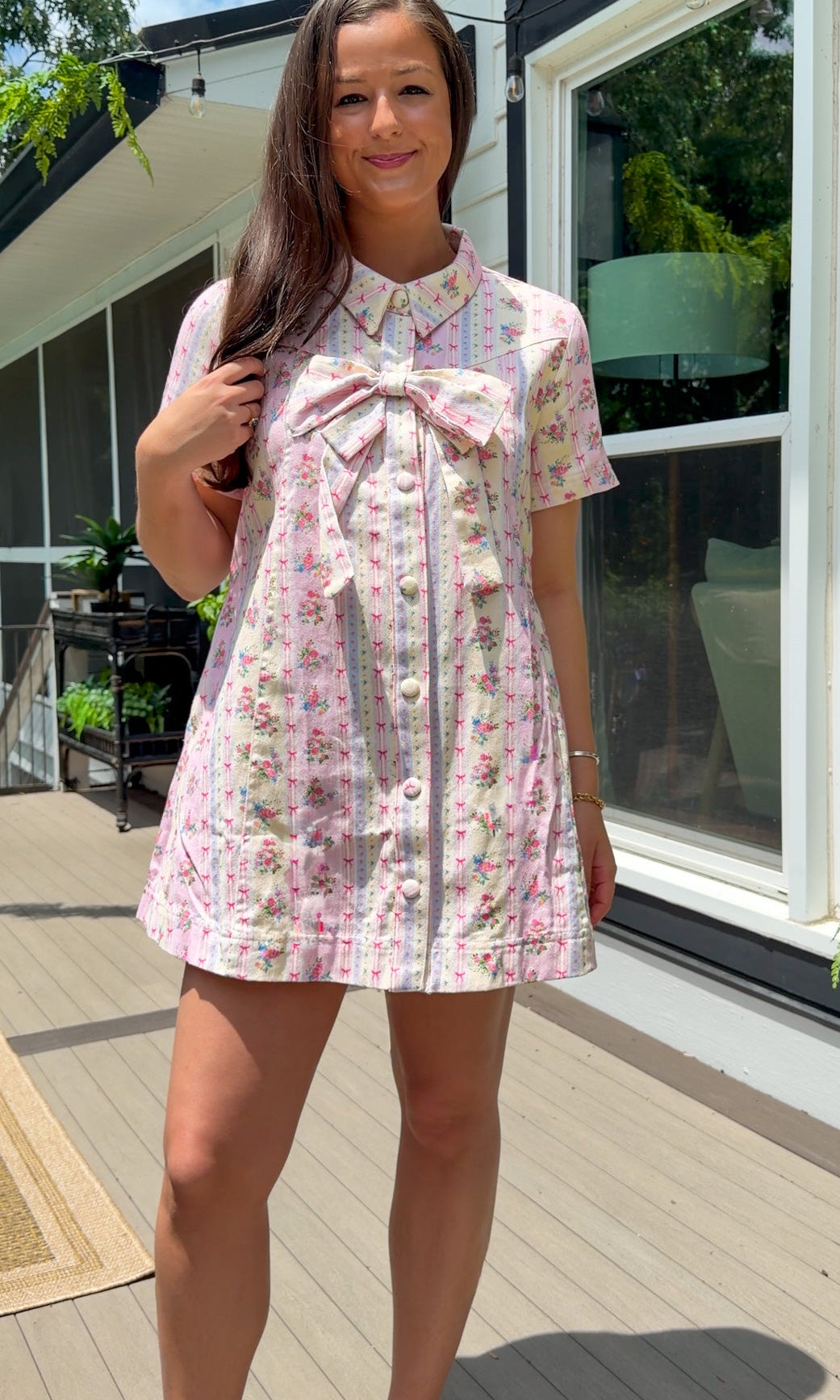 Light pink floral stripe mini dress with a collared neckline, front button closure, short sleeves, oversized bow detail, and relaxed A-line silhouette.
