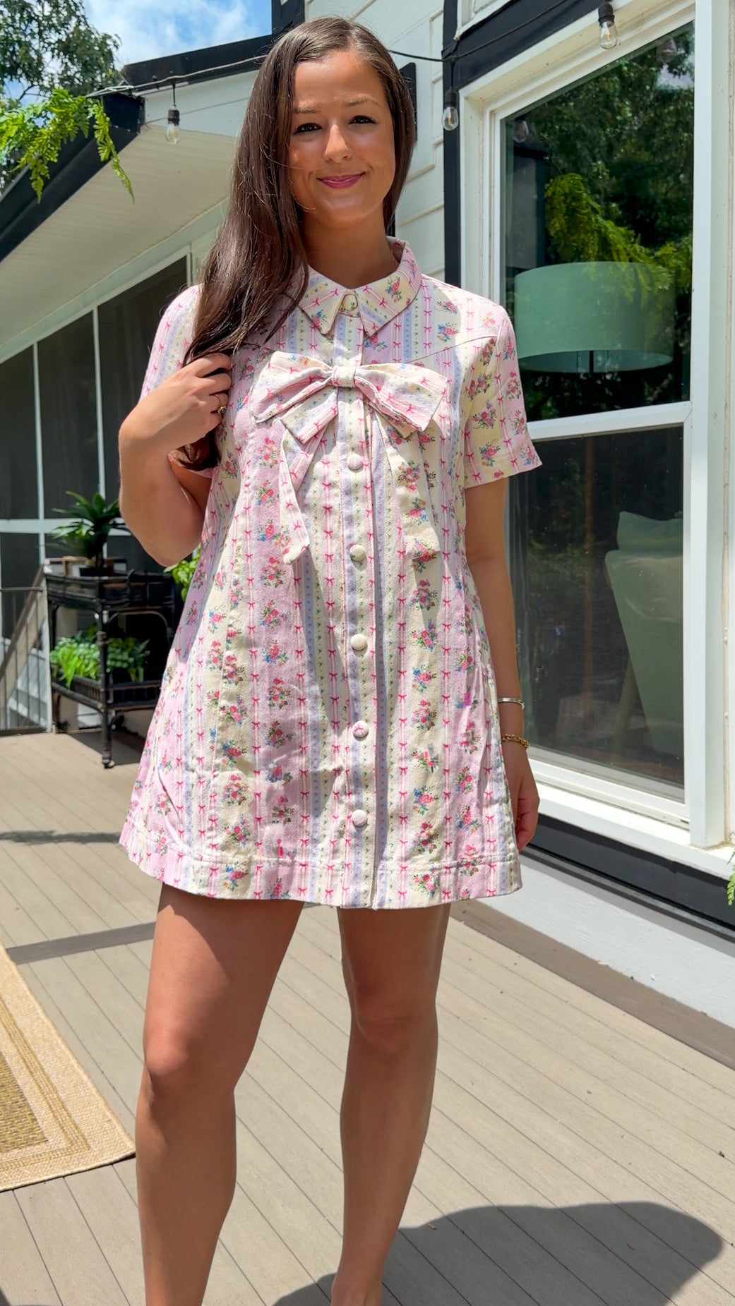 Light pink floral stripe mini dress with a collared neckline, front button closure, short sleeves, oversized bow detail, and relaxed A-line silhouette.