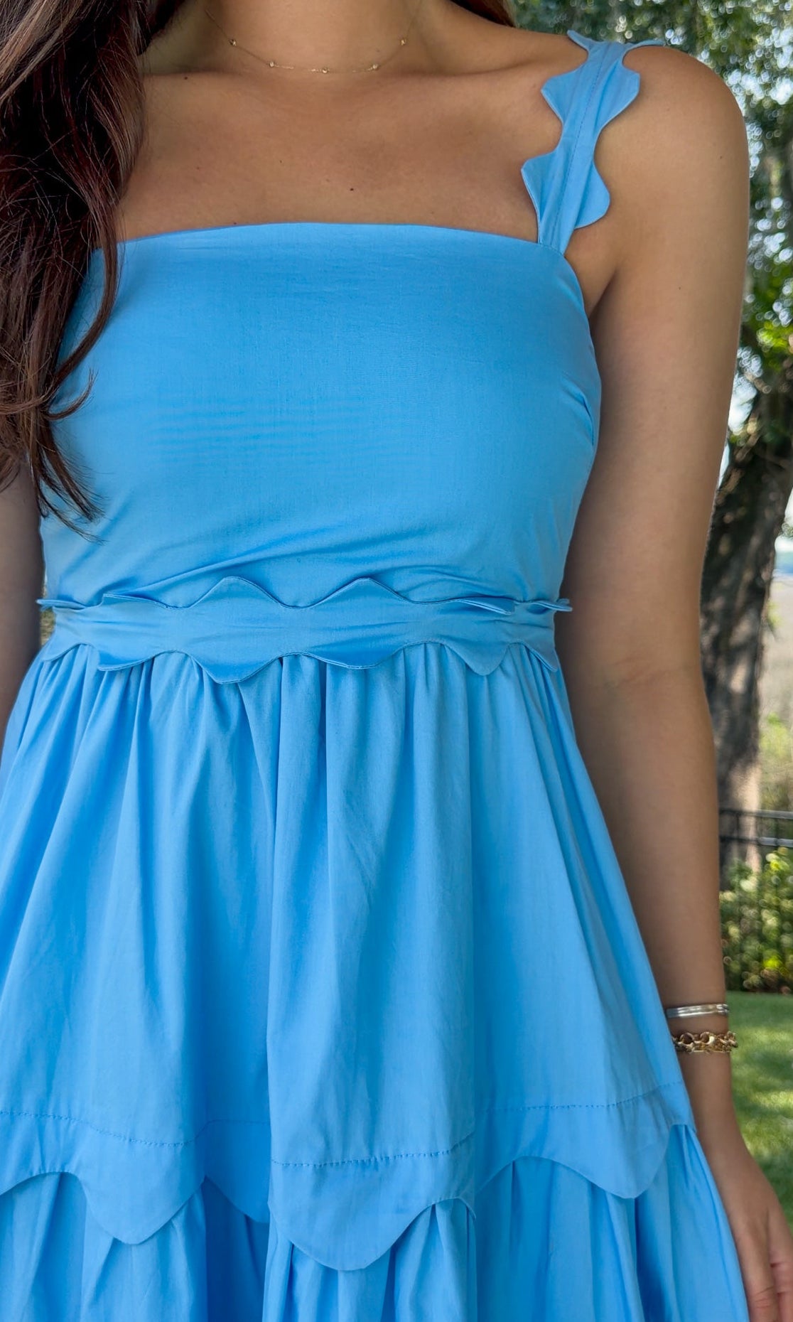 Blue midi dress featuring a square neckline, adjustable scalloped shoulder straps, scalloped trim at the empire waist and tiered skirt, a smocked back, and a flowing A-line silhouette.