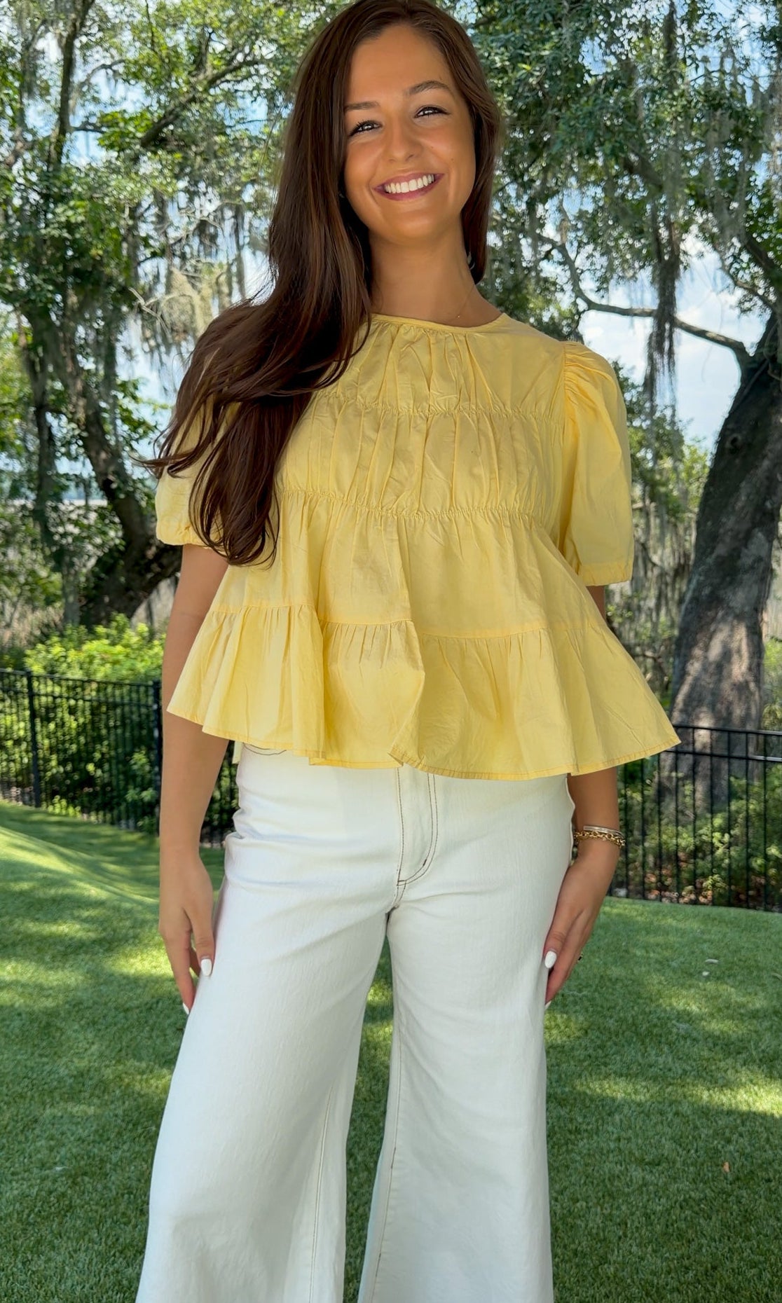 Butter yellow babydoll top featuring a round neckline, tiered shirring, short puff sleeves with adjustable tie cuffs, a ruffle-trimmed back, keyhole button closure, and a relaxed semi-cropped silhouette.