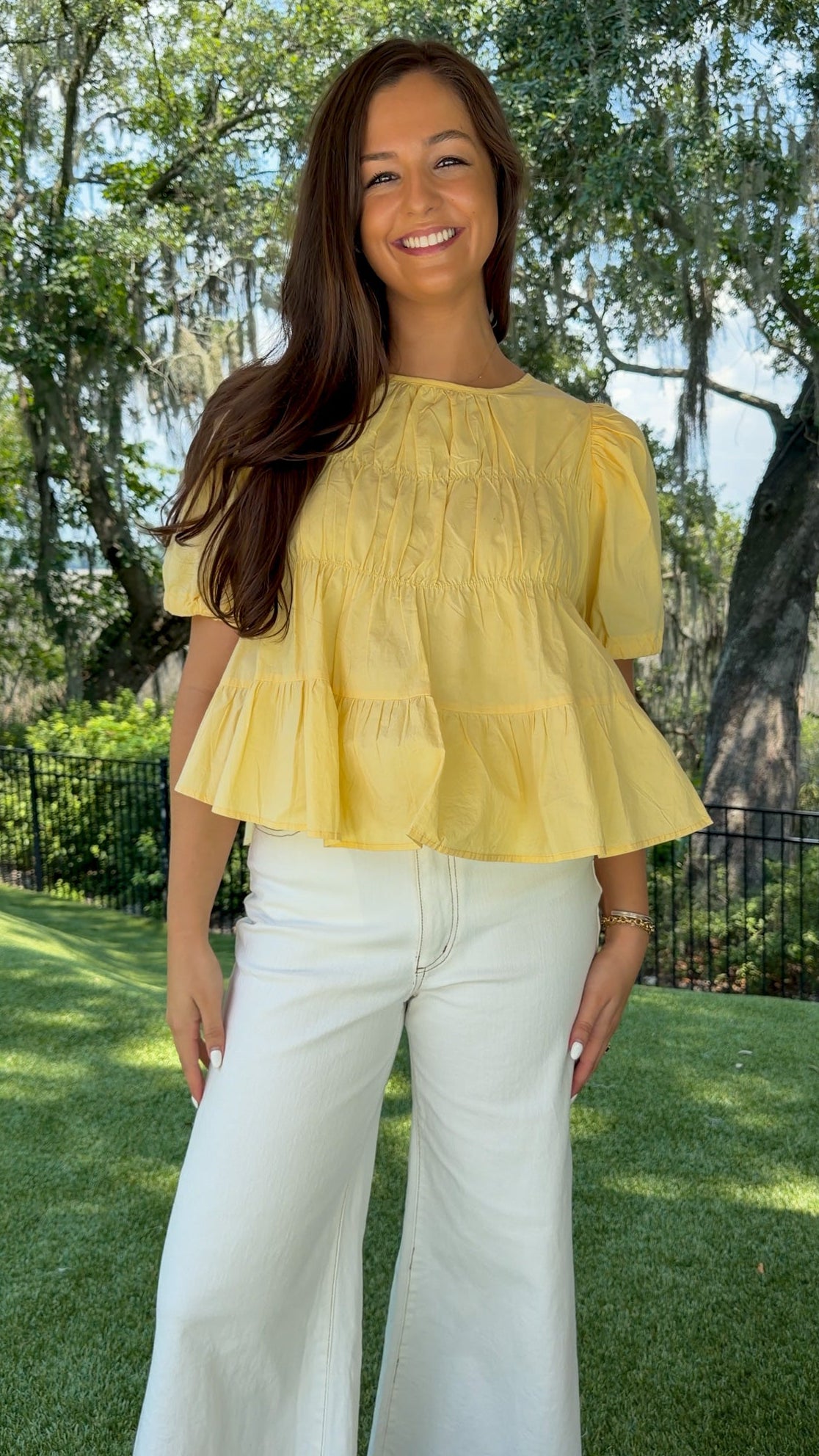 Butter yellow babydoll top featuring a round neckline, tiered shirring, short puff sleeves with adjustable tie cuffs, a ruffle-trimmed back, keyhole button closure, and a relaxed semi-cropped silhouette.