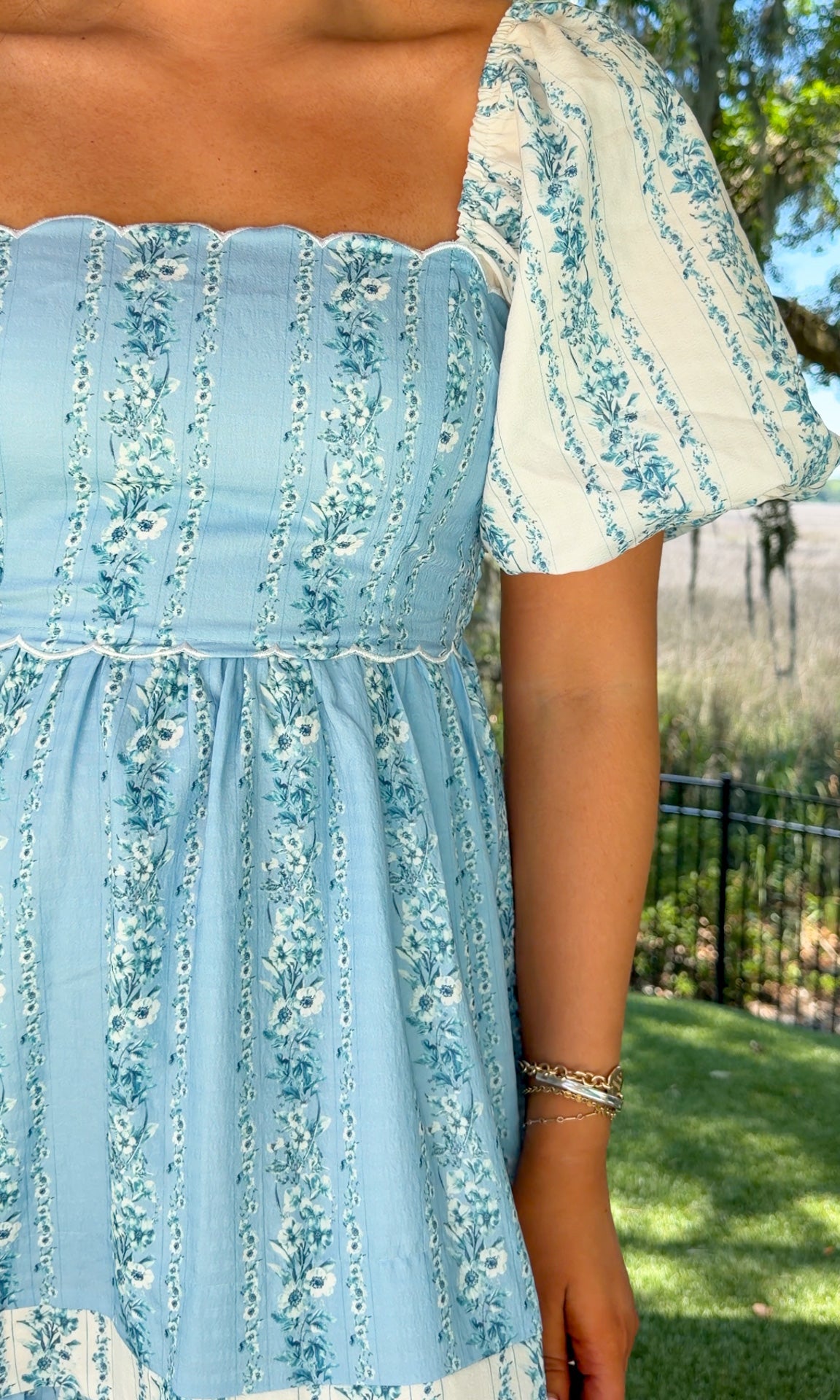 Person wearing a light blue floral dress with a blurred outdoor background
