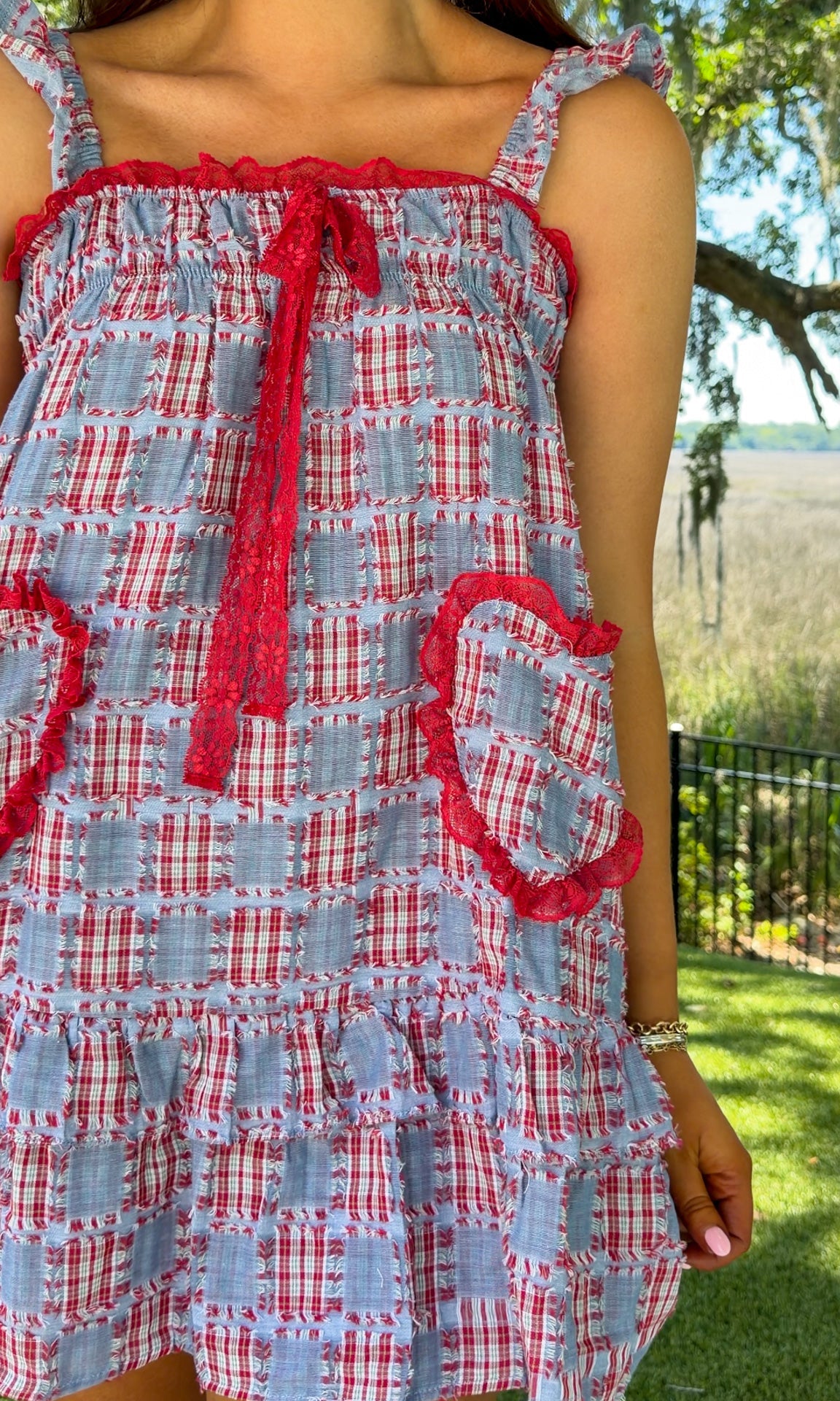Woman wearing a red, white, and blue checkered dress with ruffled details outdoors.