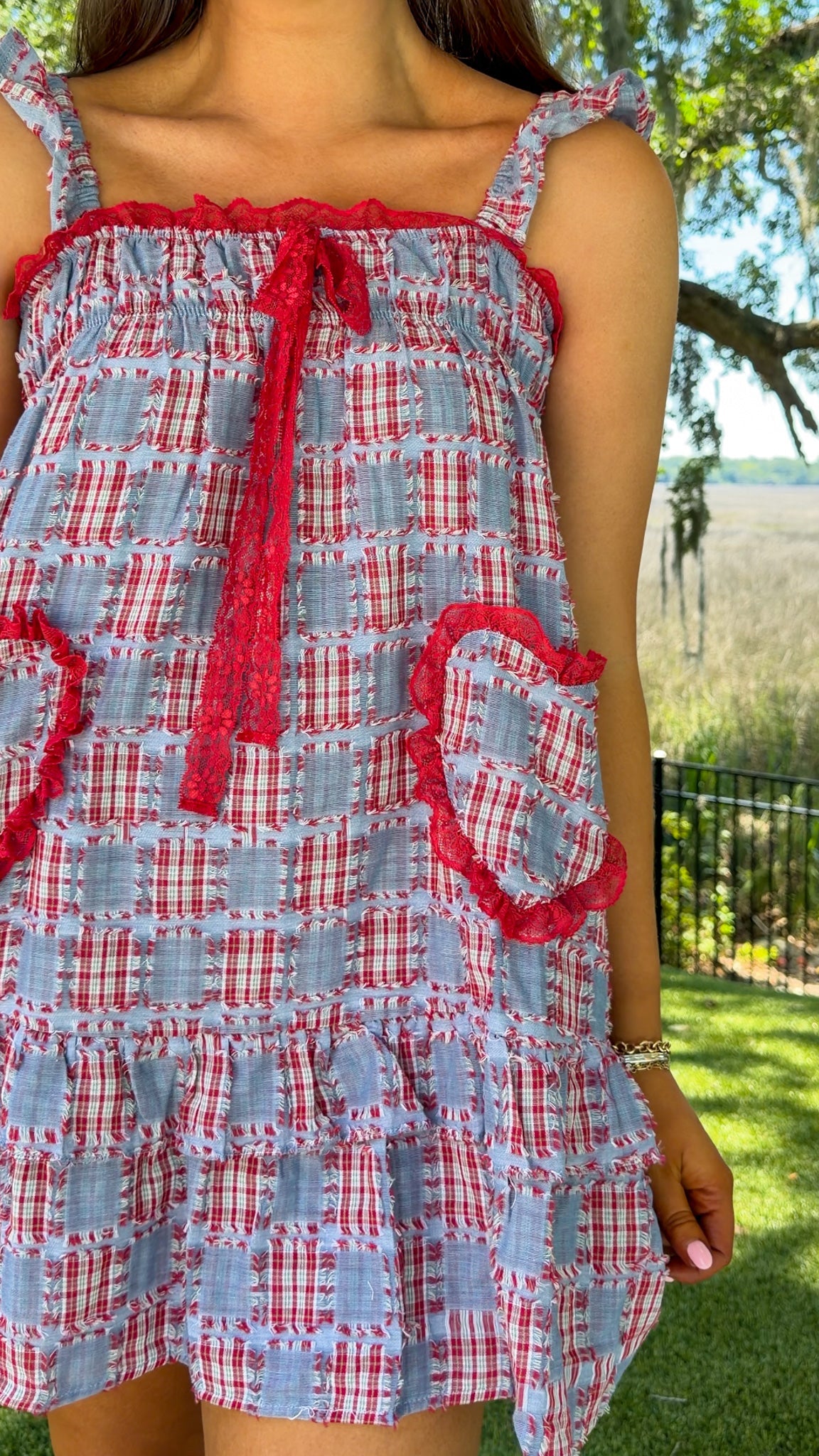 Woman wearing a red, white, and blue checkered dress with ruffled details outdoors.
