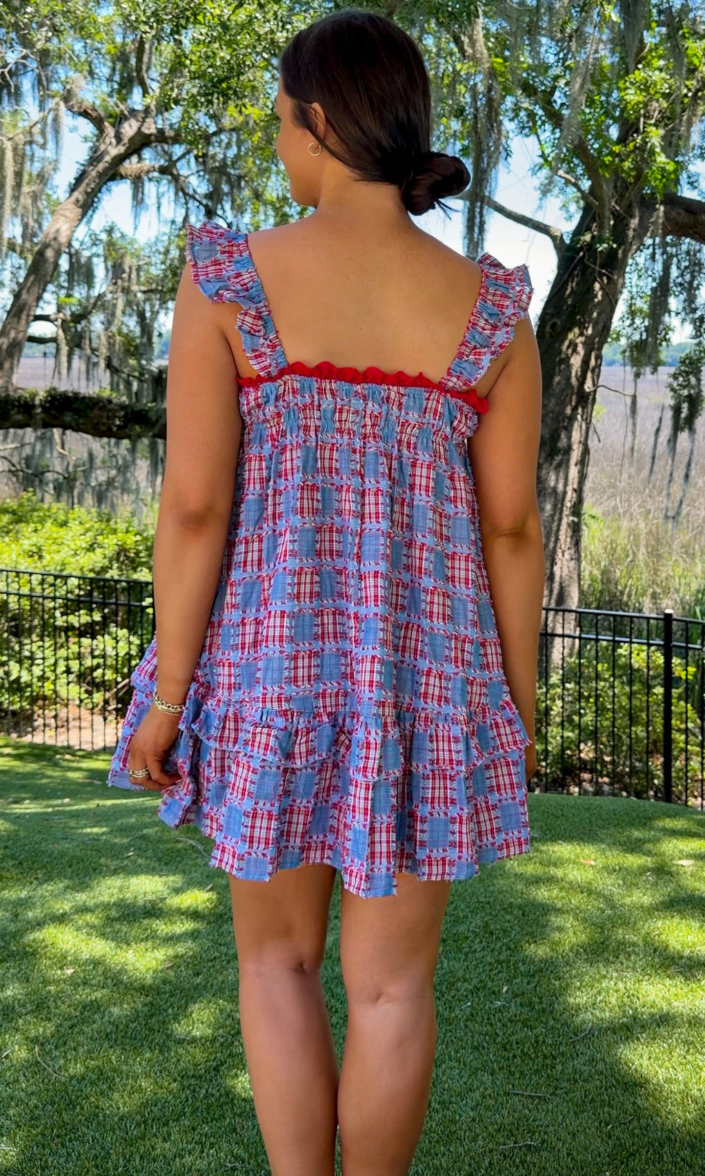 Woman wearing a blue plaid dress with red trim in a park setting