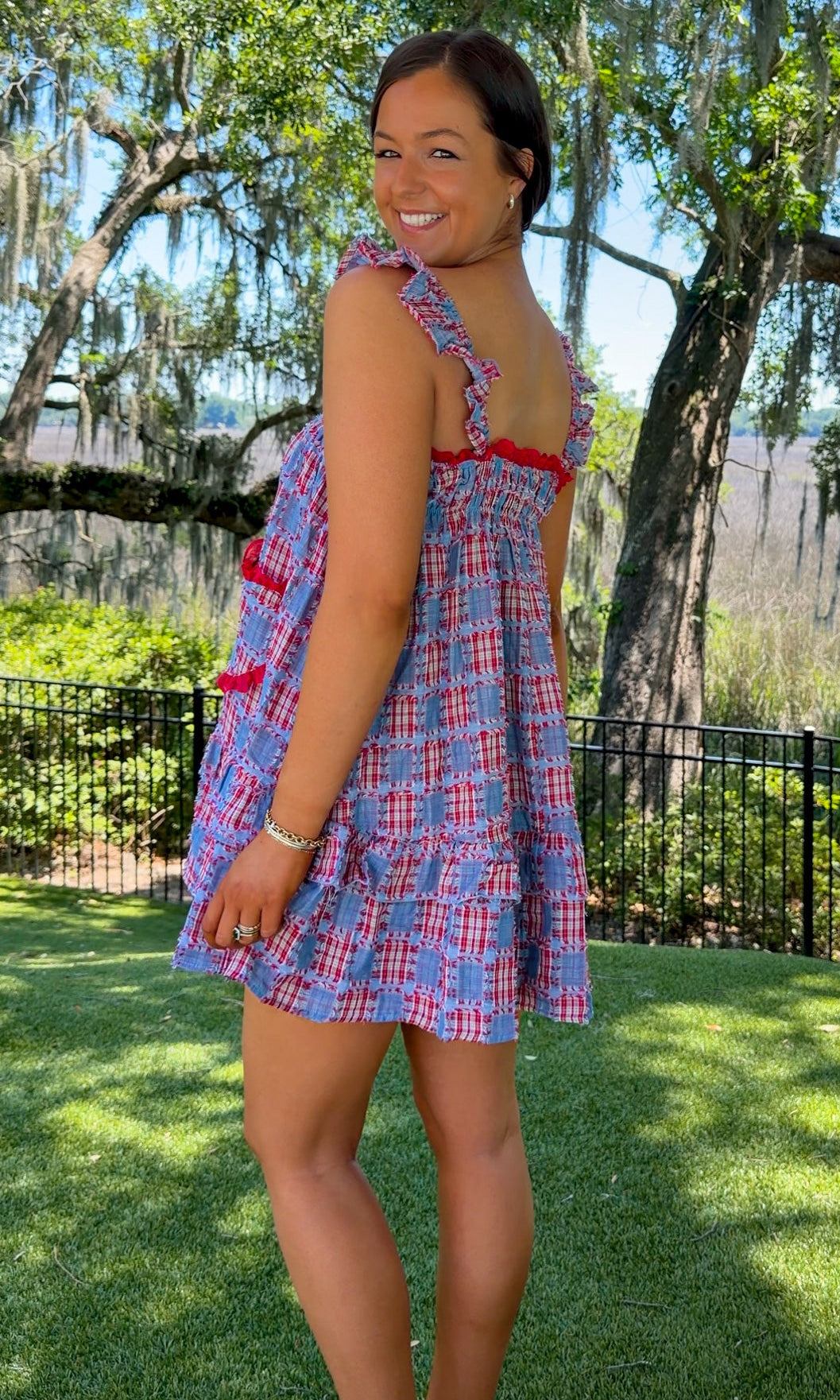 Woman in a plaid dress standing in a park with trees and grass.