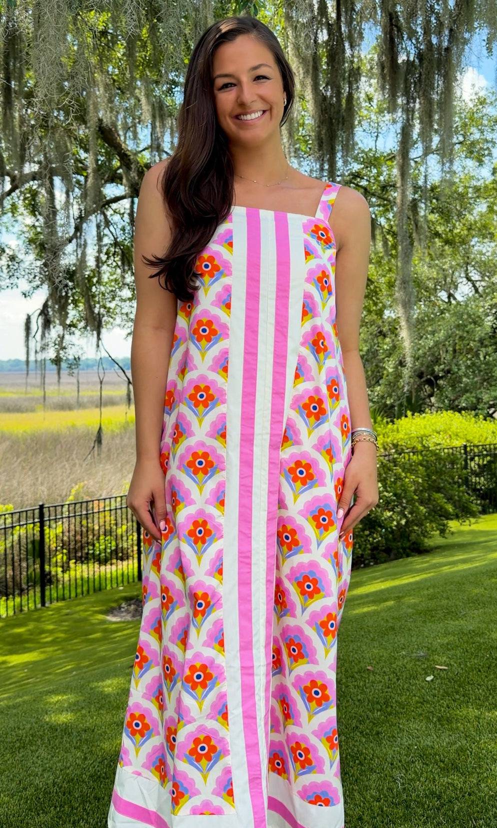 Woman in a floral dress standing outdoors with trees and grass in the background