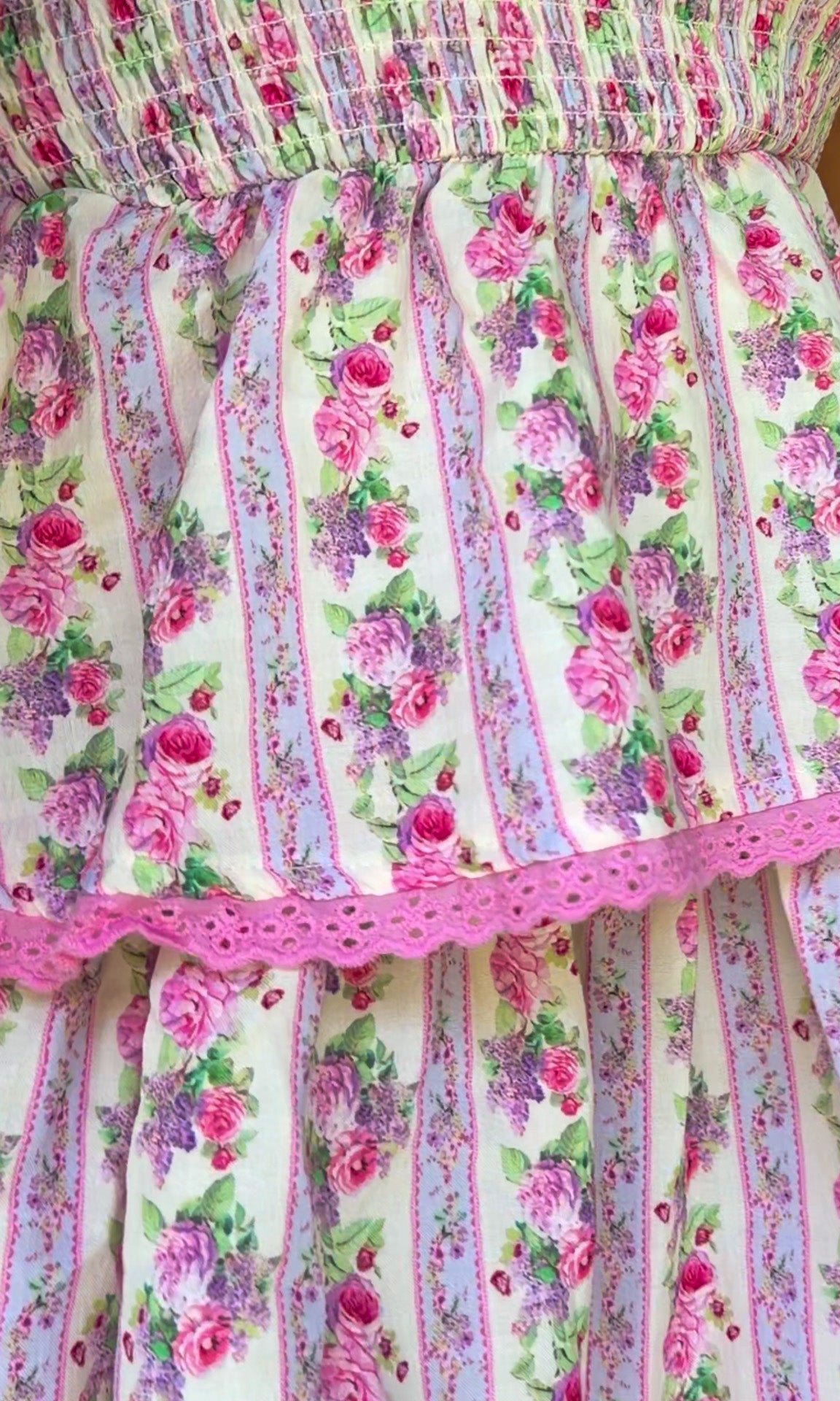 Pastel pink floral tiered mini dress with a smocked bodice, adjustable shoulder tie straps, lace trim detailing, and a flowy tiered skirt.