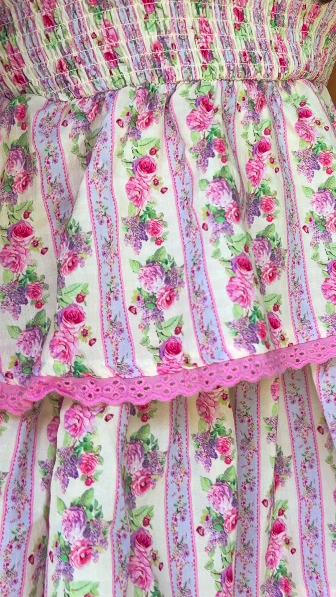 Pastel pink floral tiered mini dress with a smocked bodice, adjustable shoulder tie straps, lace trim detailing, and a flowy tiered skirt.
