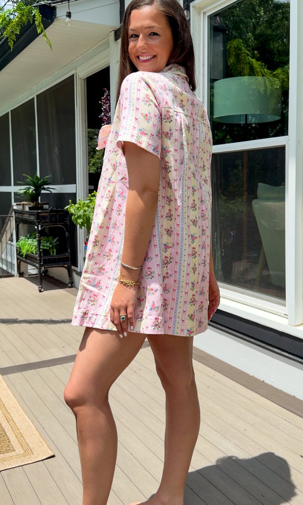 Light pink floral stripe mini dress with a collared neckline, front button closure, short sleeves, oversized bow detail, and relaxed A-line silhouette.